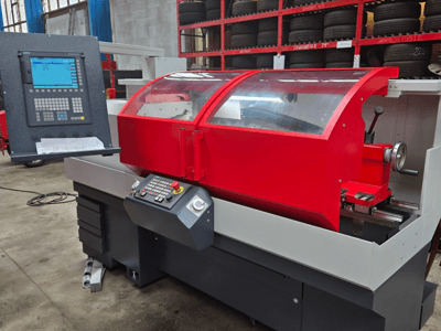 Tornio CNC rosso con pannello di controllo, vista frontale; dotato di coperchio trasparente, portautensili e cassetti di stoccaggio.