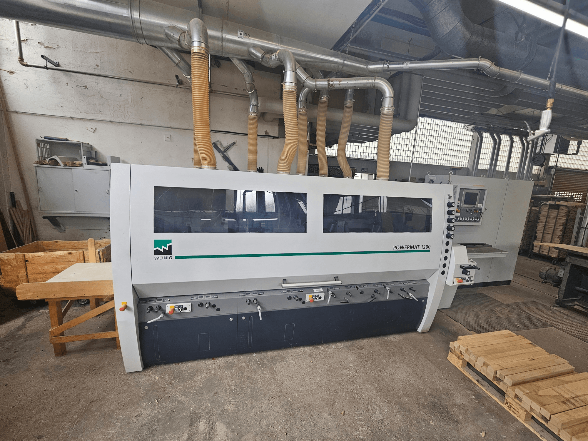 Macchina per la lavorazione del legno Weinig Powermat 1200, vista frontale, con pannello di controllo e cataste di legno in un'officina.