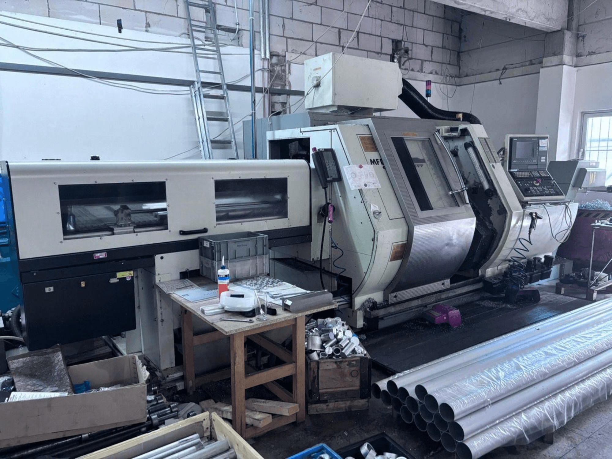 Centro di tornitura e fresatura Gildemeister MF Twin 65, vista laterale che mostra il pannello di controllo, l'area di lavorazione e i tubi in alluminio.