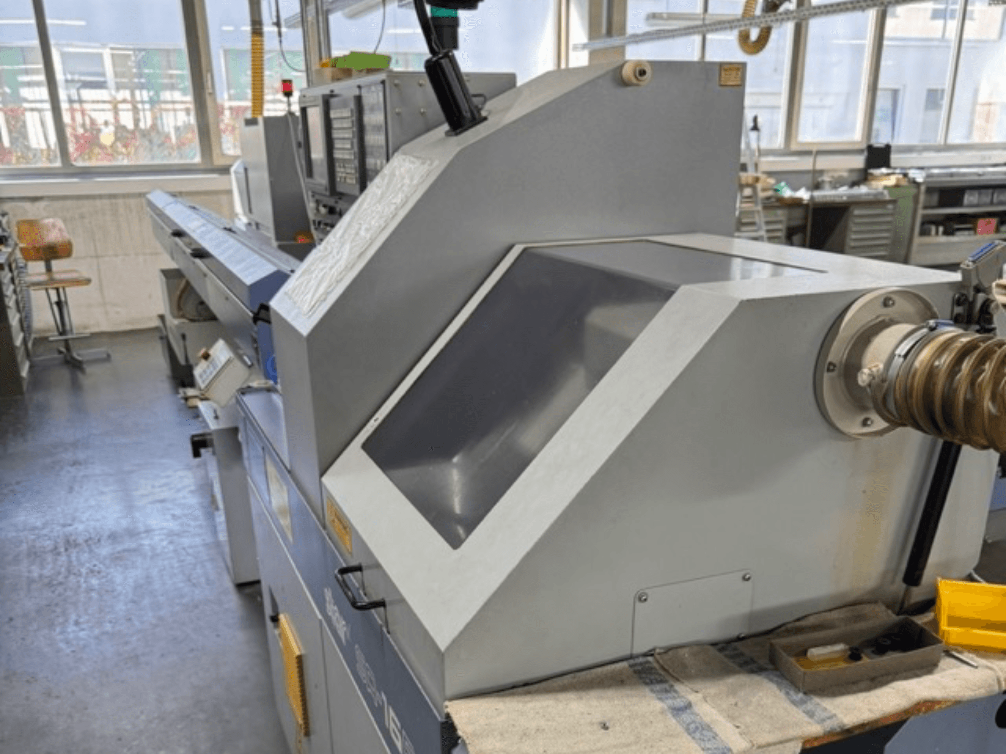 Macchina industriale grigia vista di lato, presenta un ampio pannello angolato, pulsanti di controllo e un attacco per il tubo flessibile.