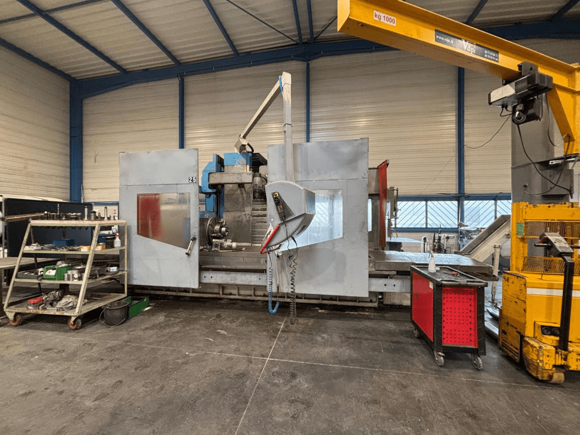 Fresatrice CNC vista di lato in un'officina; strumenti e ripiani di stoccaggio visibili. Marca e modello non specificati.