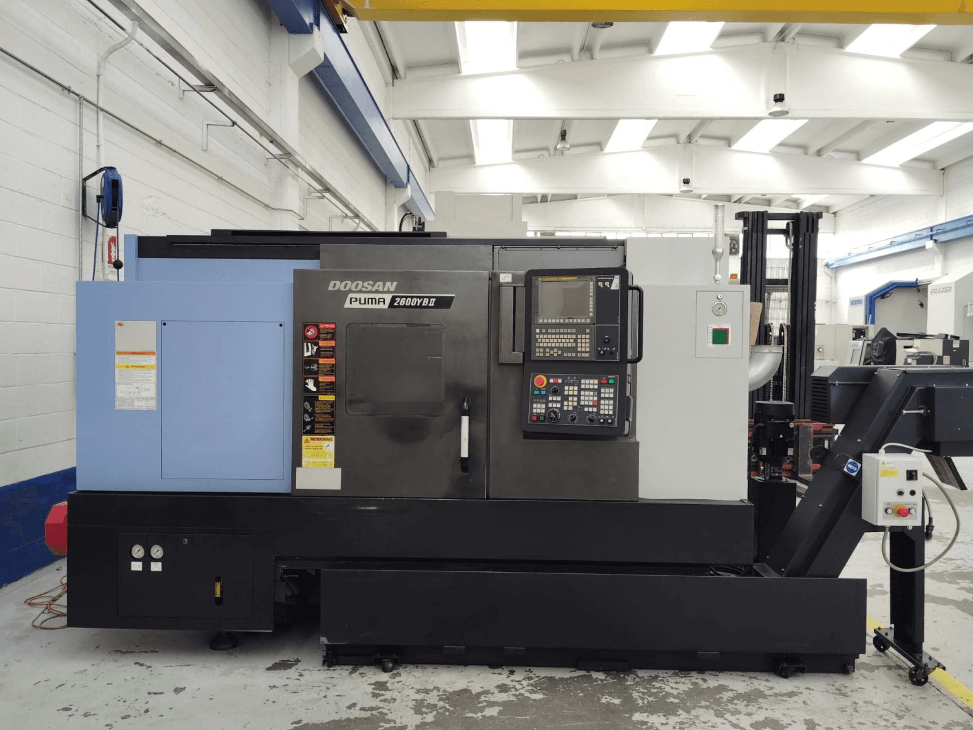 Vista frontale del tornio orizzontale DOOSAN Puma 2600YB II con pannello di controllo ed etichette di sicurezza visibili.