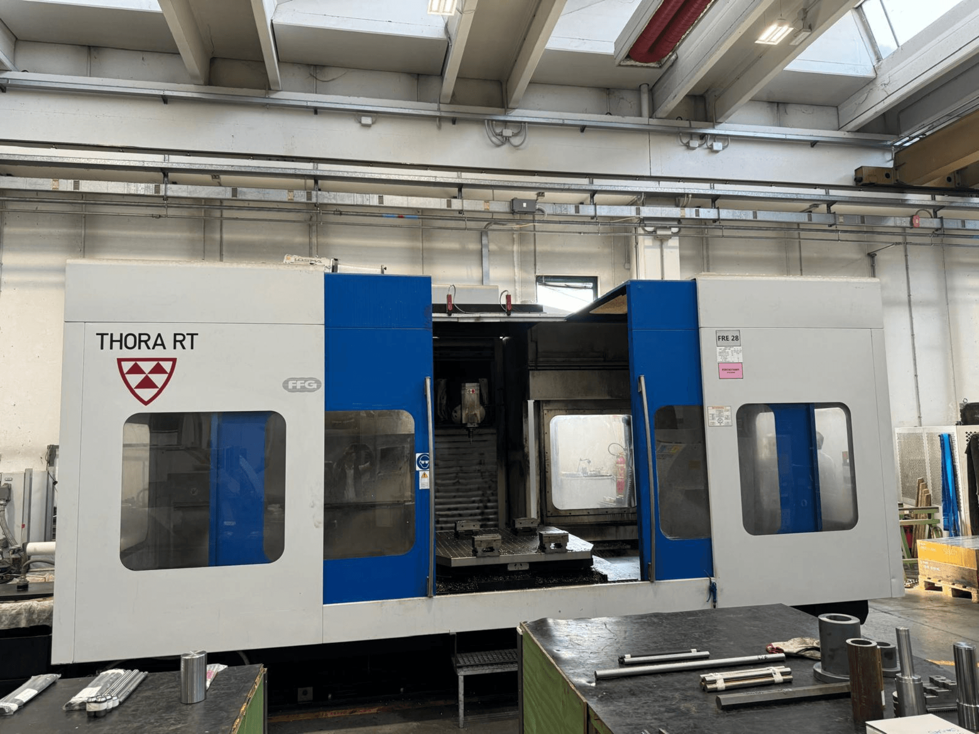 Macchina CNC THORA RT vista frontalmente, con esterno blu e bianco, finestre trasparenti e utensili montati.