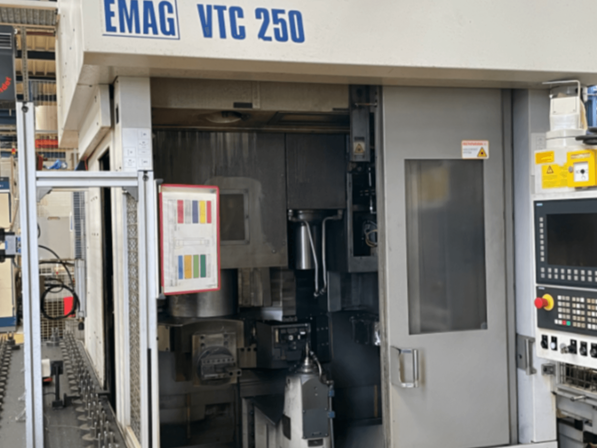 Vista frontale del tornio verticale EMAG VTC 250, con pannello di controllo, interfaccia operativa e sportello di accesso aperto.