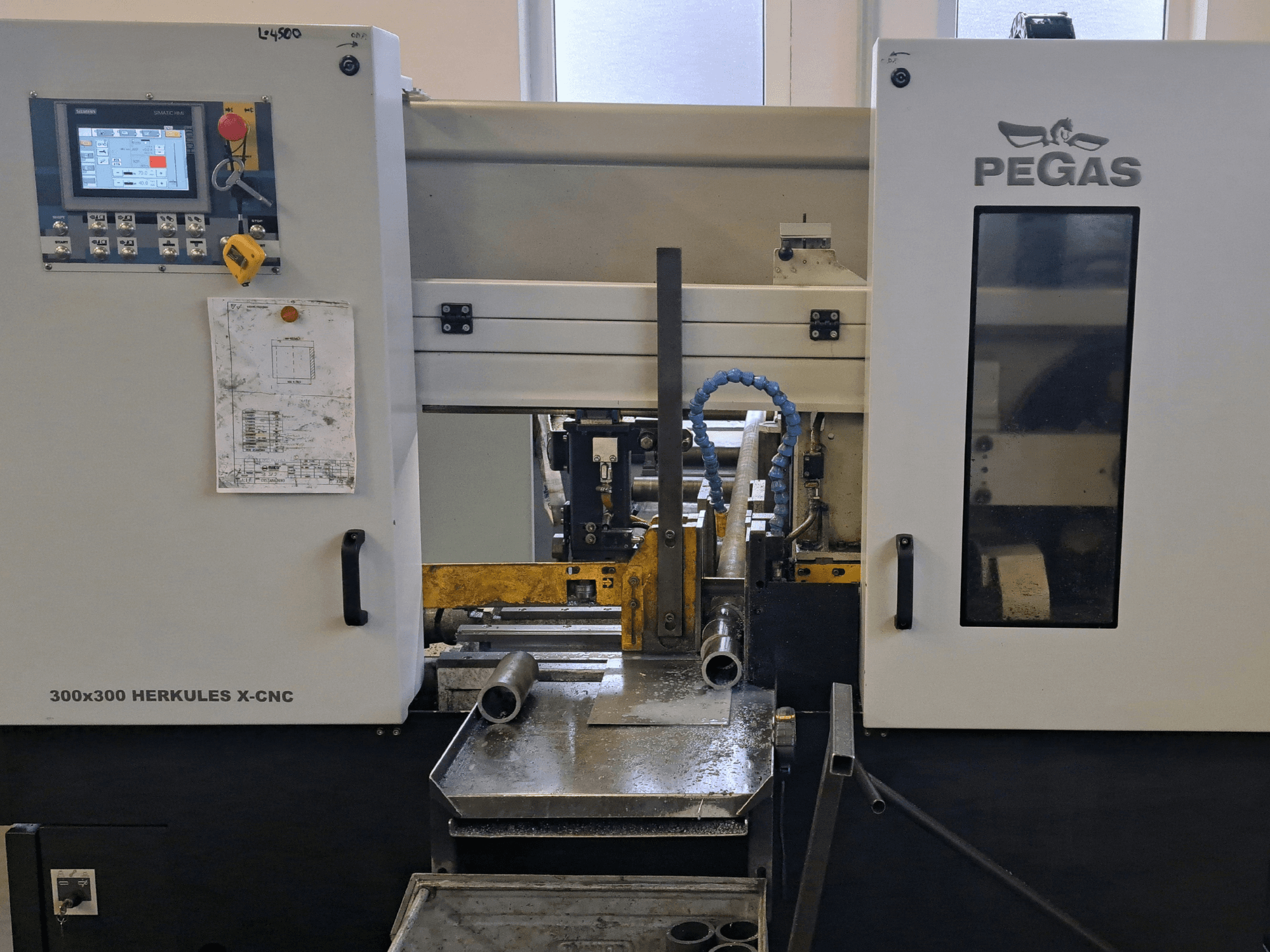 Macchina per la lavorazione della lamiera Pegas HERKULES X-CNC 300x300, vista frontale, che mostra il pannello di controllo e l'area di lavoro con i pezzi di metallo.