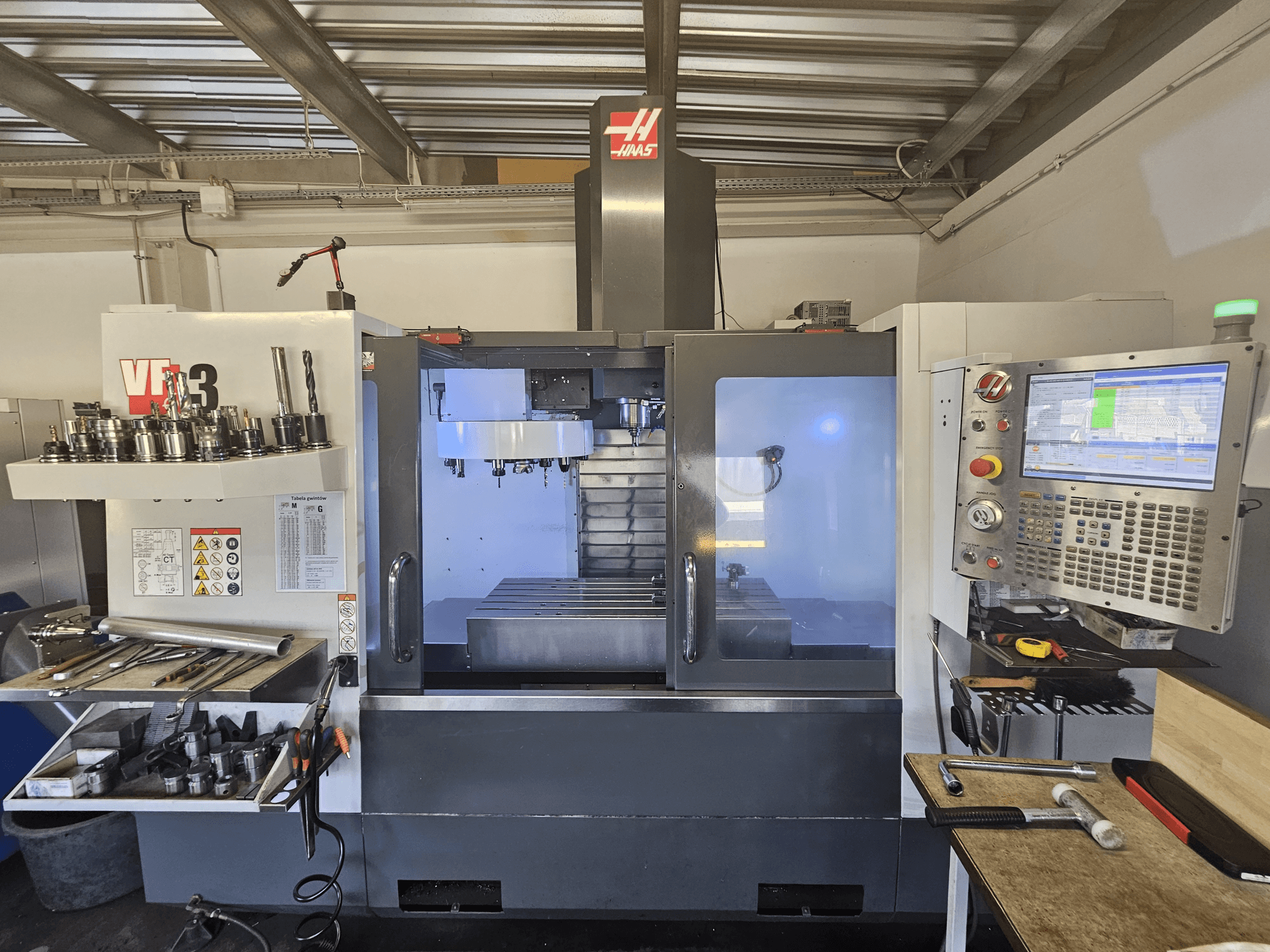 Macchina CNC Haas VF-3 in un'officina, vista frontale che mostra utensili, comandi e area di fresatura con interno illuminato.