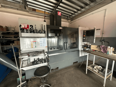 Macchina CNC Haas VF-3 in officina, vista frontale con utensili e comandi sul tavolo adiacente, con visualizzazione dell'interfaccia tecnica e delle informazioni sulla sicurezza.