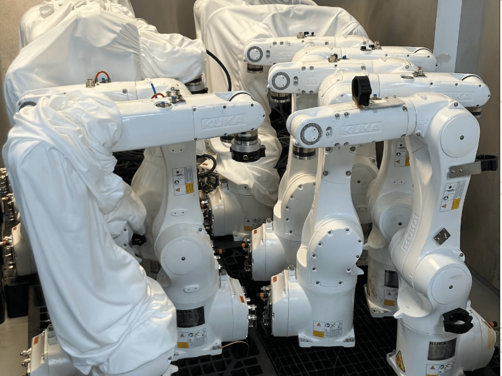 Bracci robotici KUKA KR 10 R900-2 rivestiti in tessuto bianco, visti da un'angolazione dall'alto, che mostrano più unità in magazzino.