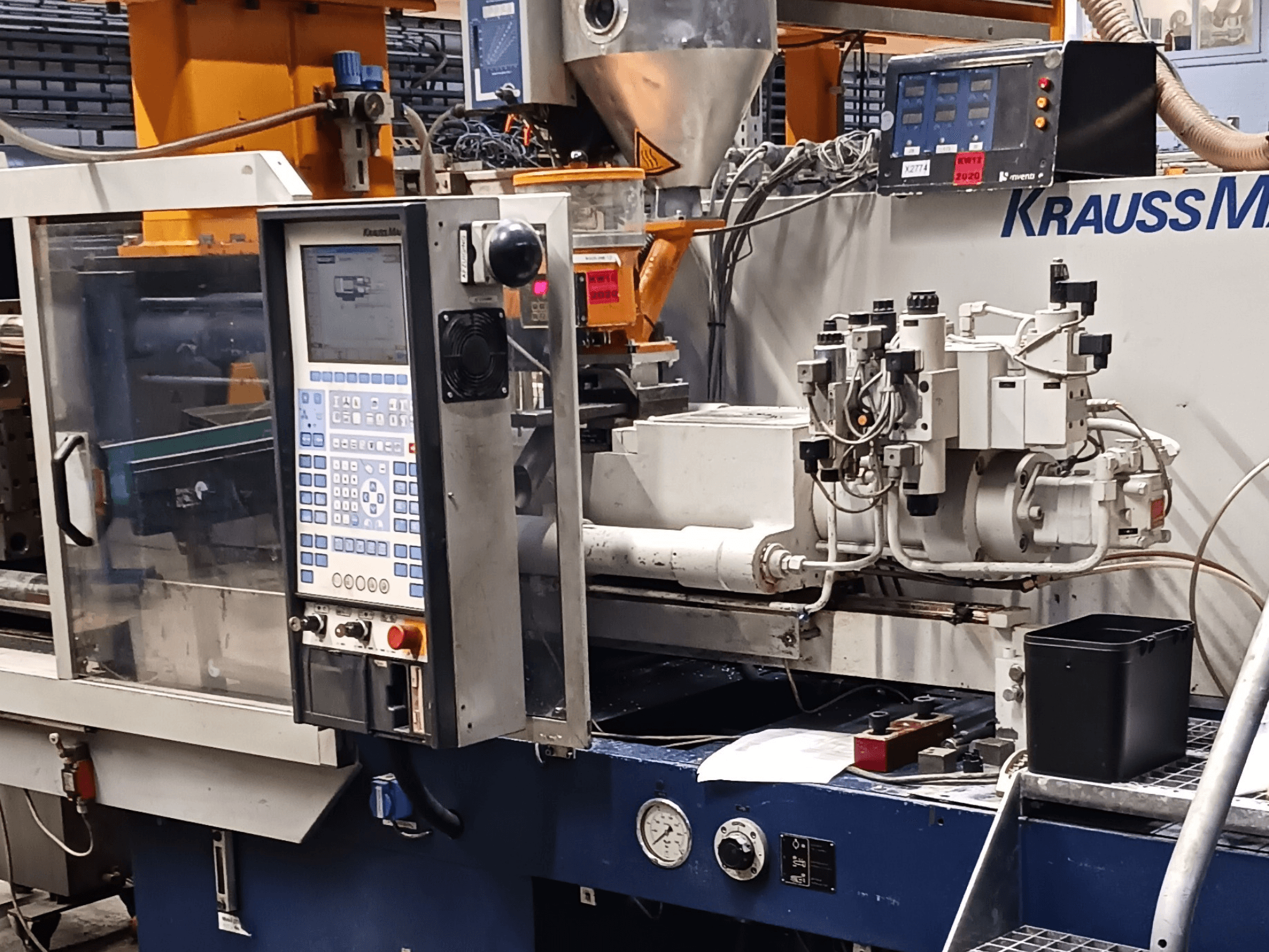 Macchina ad iniezione KraussMaffei con pannello di controllo, unità idrauliche e utensili in primo piano, vista frontale.