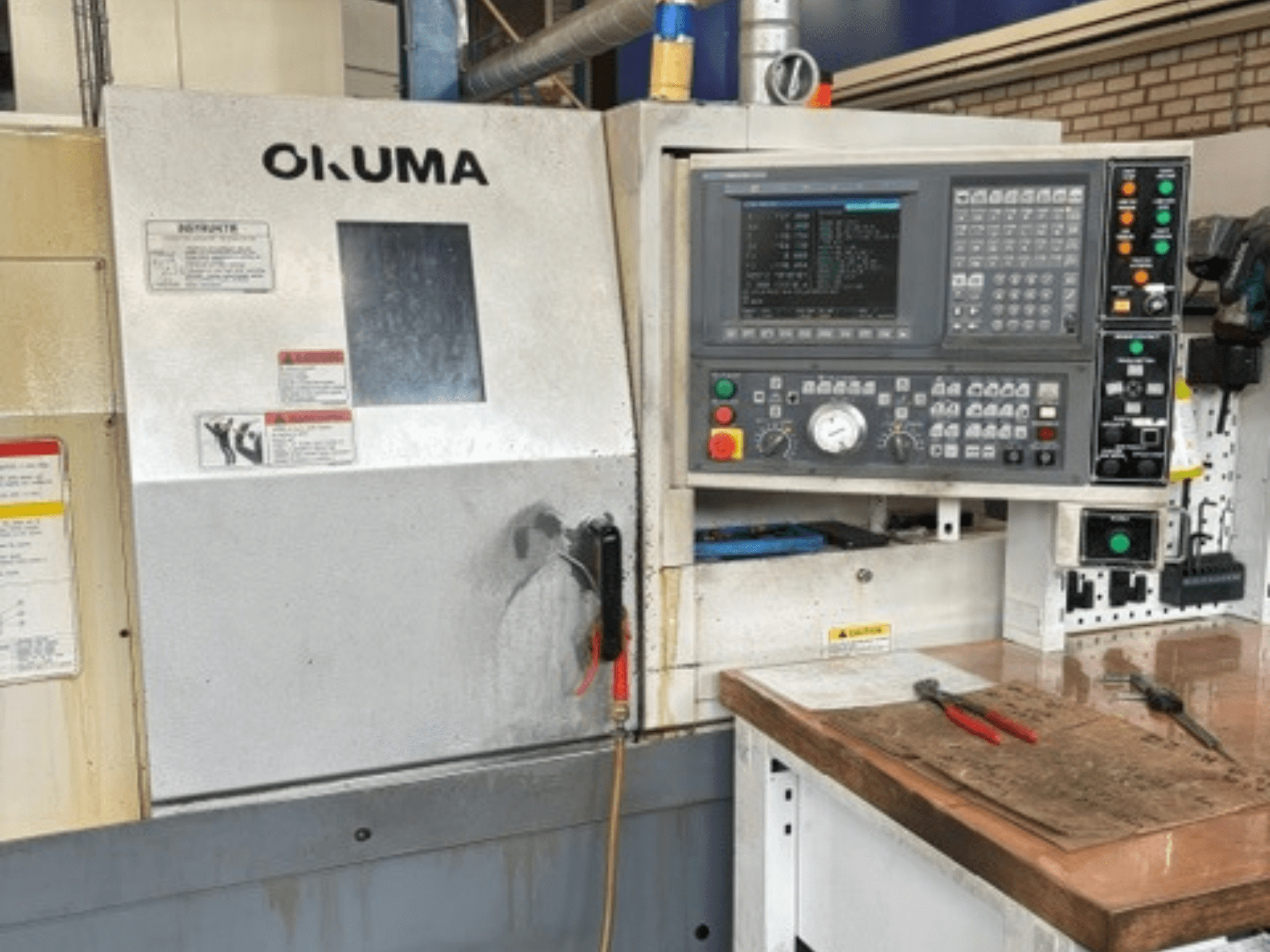 Vista frontale del tornio orizzontale Okuma ES-L10II, con pannello di controllo, display e area di lavoro con utensili.