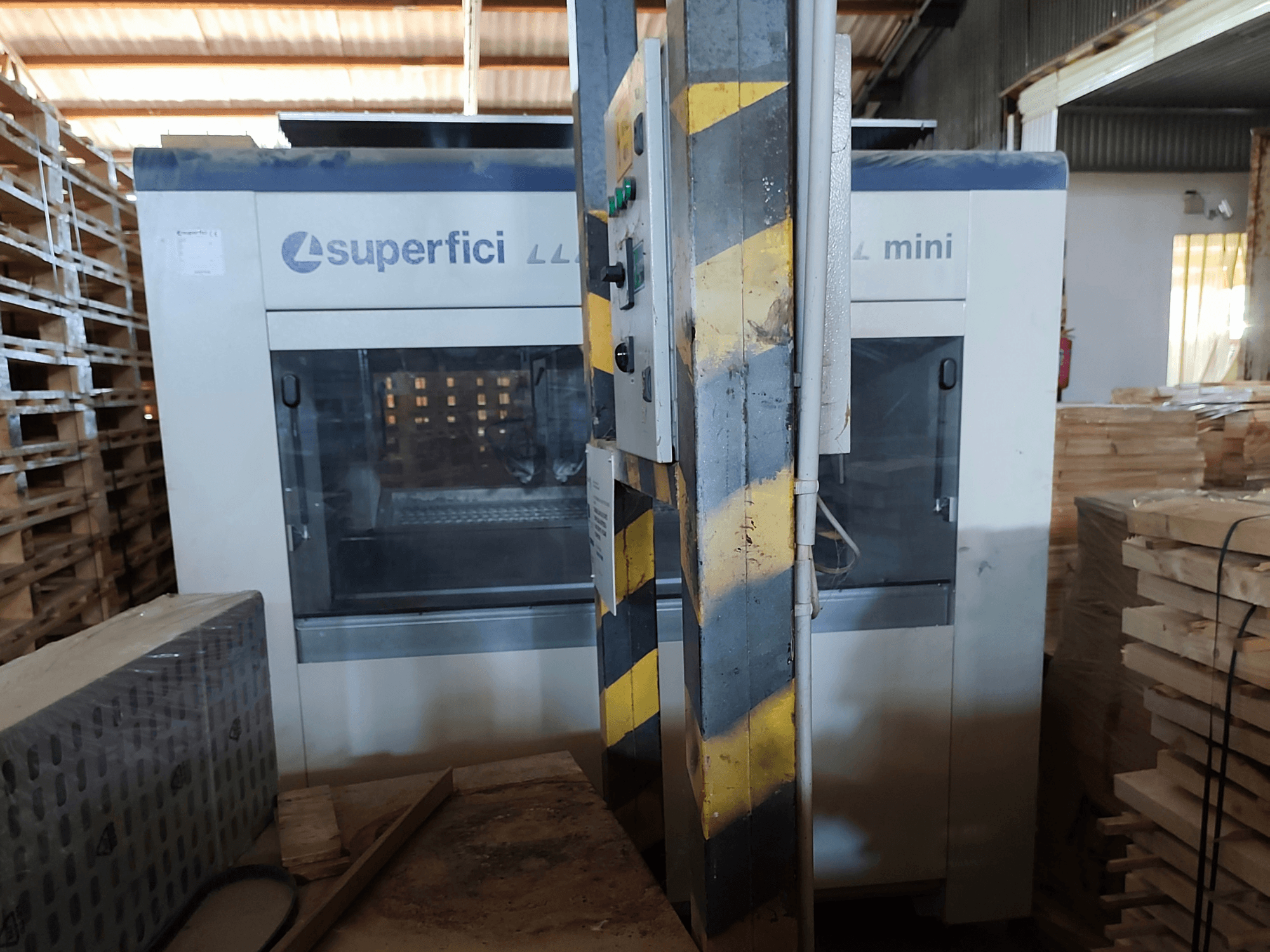 Macchina per la finitura del legno SCM Superfici Mini vista frontale, con il pannello di controllo e i pallet di legno circostanti.