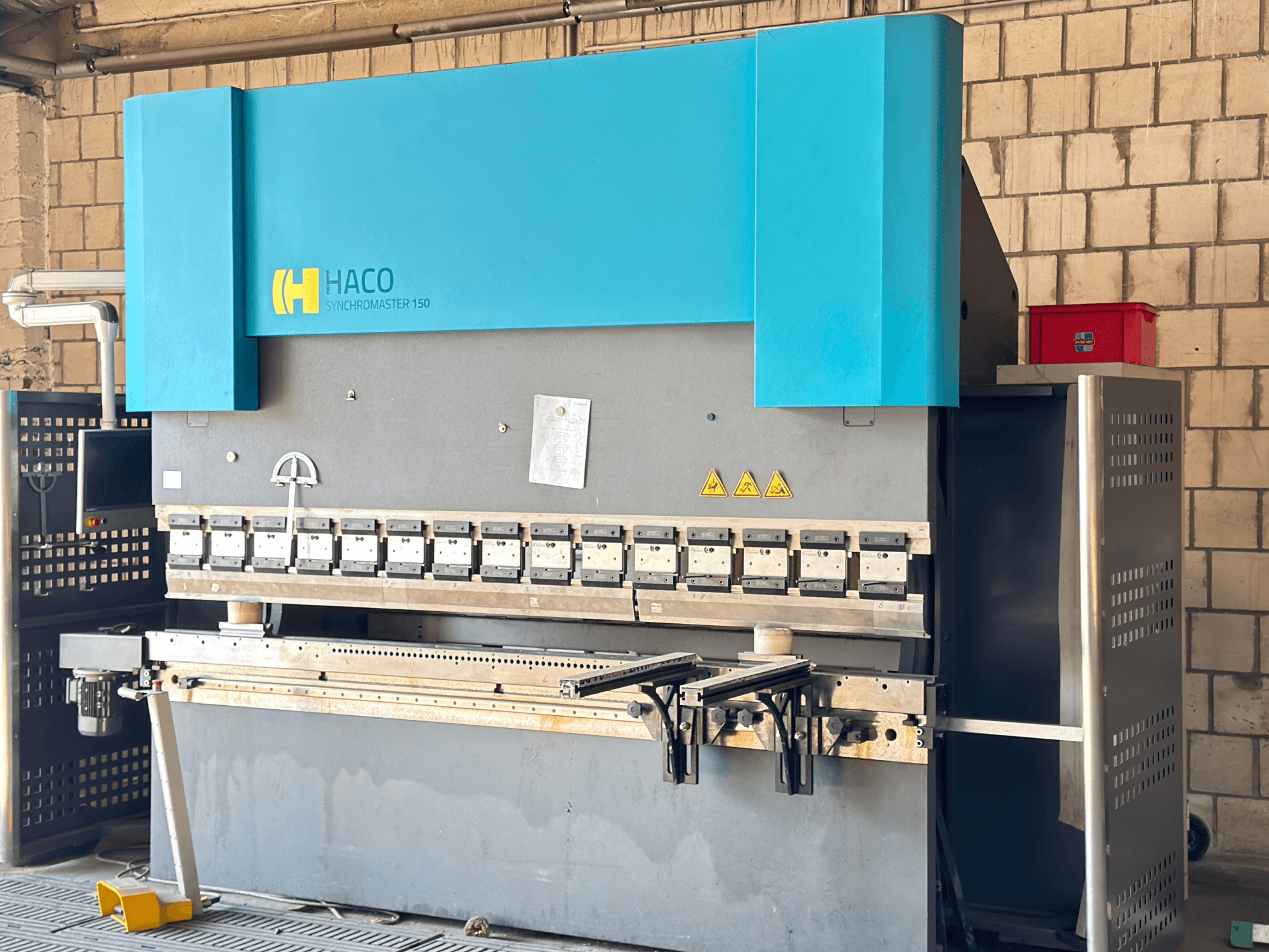 Pressa piegatrice HACO SRM30150, vista frontale; include il pannello di controllo e gli stampi di bloccaggio, con etichette di sicurezza visibili.