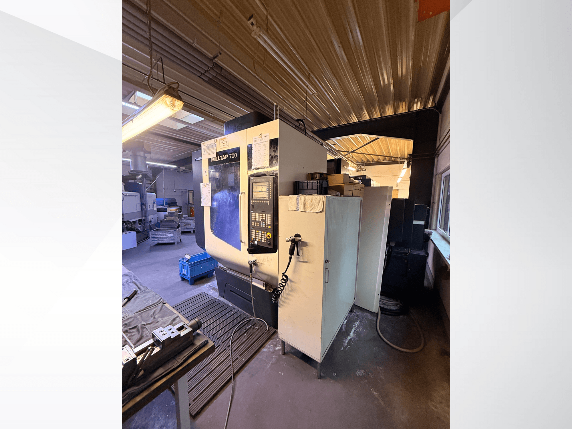 Macchina CNC Milltap 700 in officina; la vista frontale mostra il pannello di controllo, le rastrelliere degli utensili e le aree di stoccaggio con l'illuminazione sovrastante.