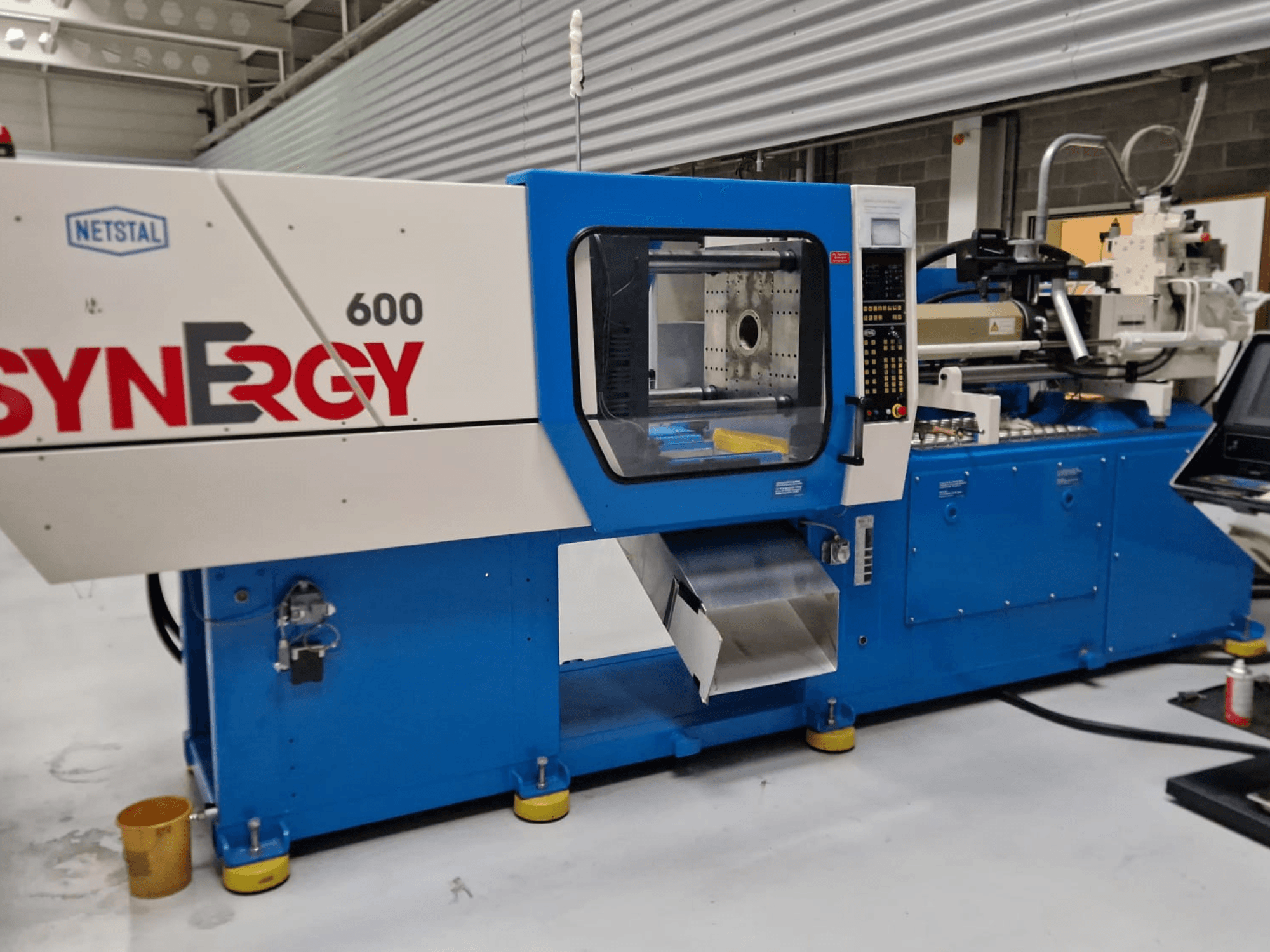 Pressa a iniezione idraulica Netstal Synergy 600-230, vista laterale che mostra il pannello di controllo e l'area di iniezione.