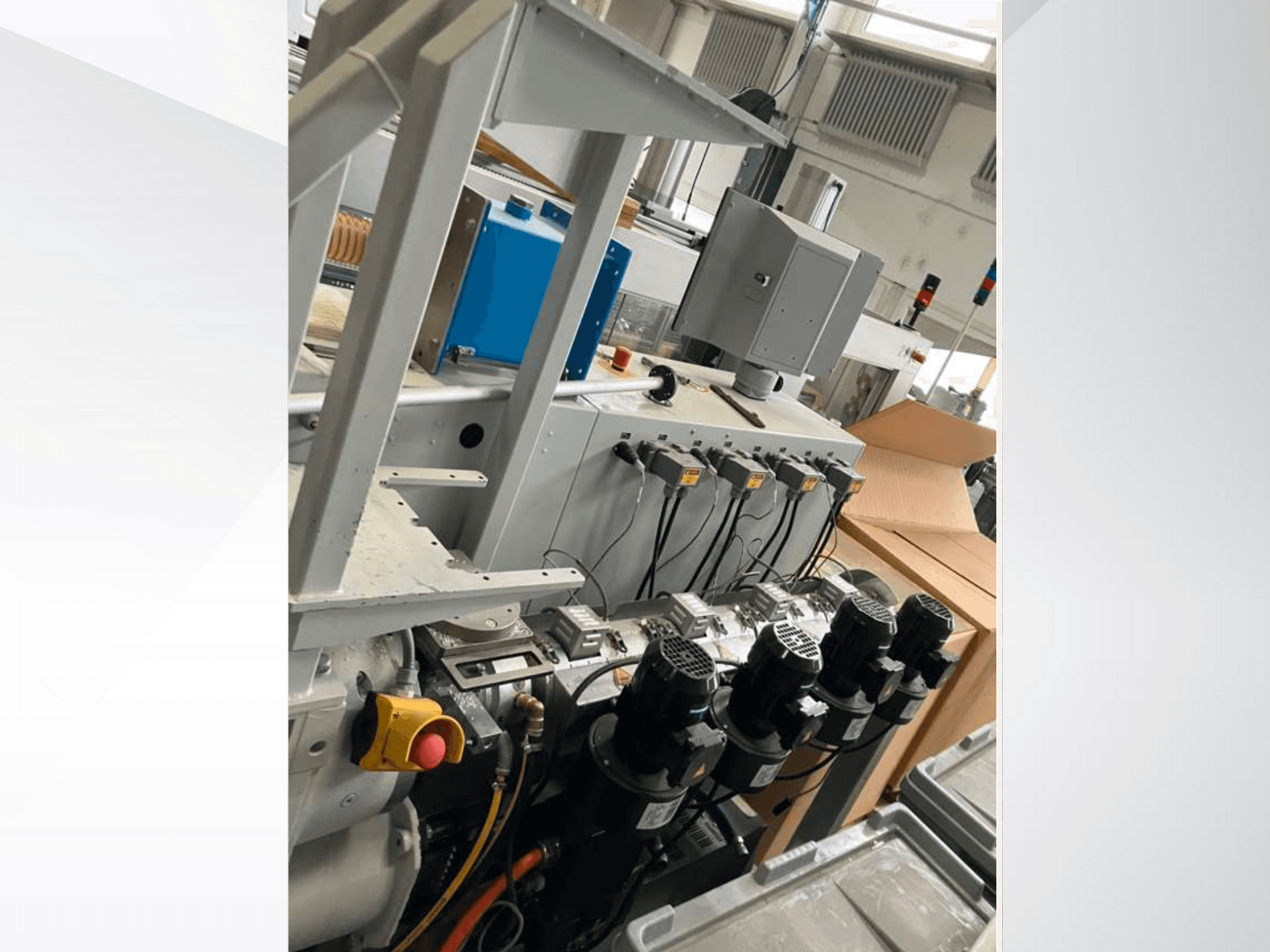 Pannello di controllo di un macchinario industriale con più motori, indicatori e un monitor; vista laterale all'interno di una fabbrica.