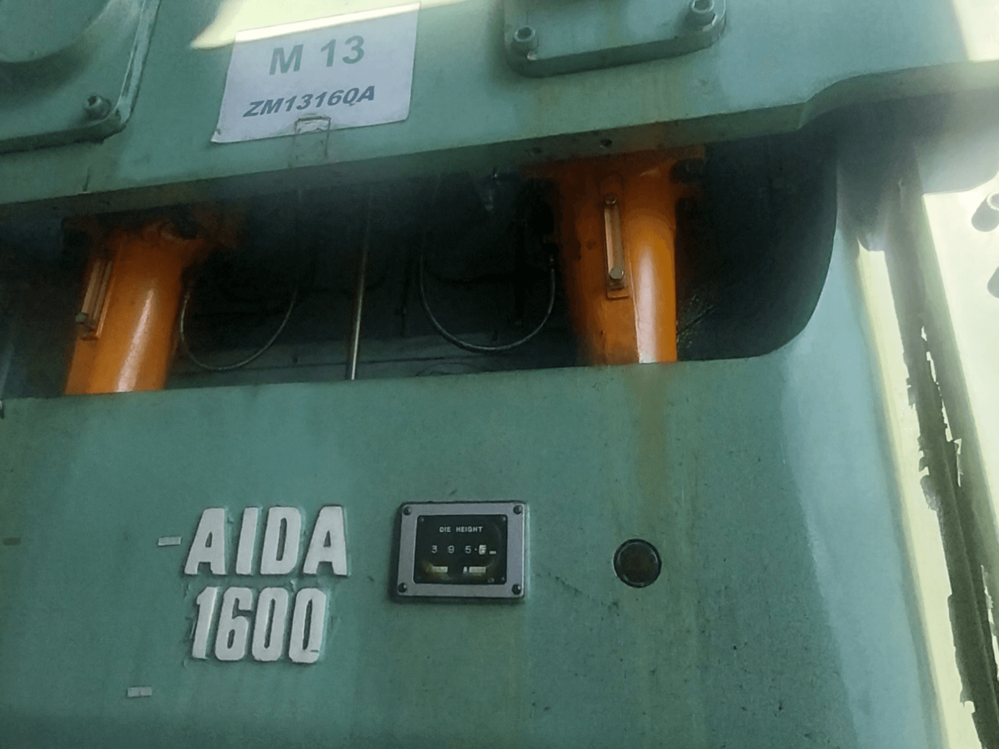 Pressa di tranciatura meccanica AIDA NC2-1600, vista frontale; visibili i componenti idraulici arancioni e il misuratore dell'altezza dello stampo.
