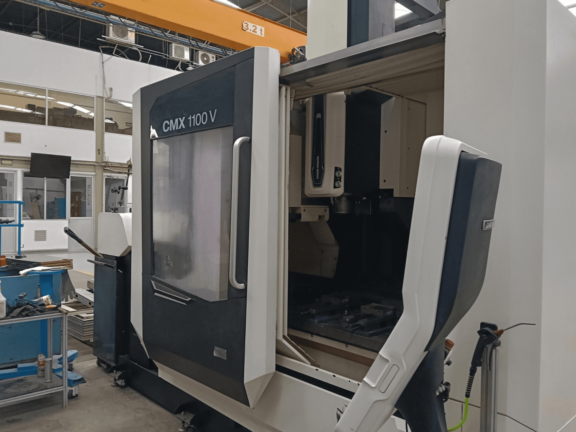 Centro di lavorazione verticale DMG MORI CMX 1100 V, vista frontale con porta aperta e configurazione interna degli utensili in un ambiente industriale.