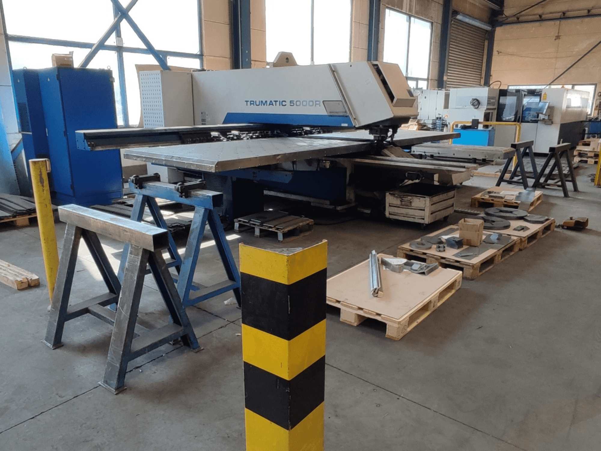 Punzonatrice CNC TRUMPF Trumatic 5000 R in un'officina, vista laterale con utensili e materiali su pallet nelle vicinanze.