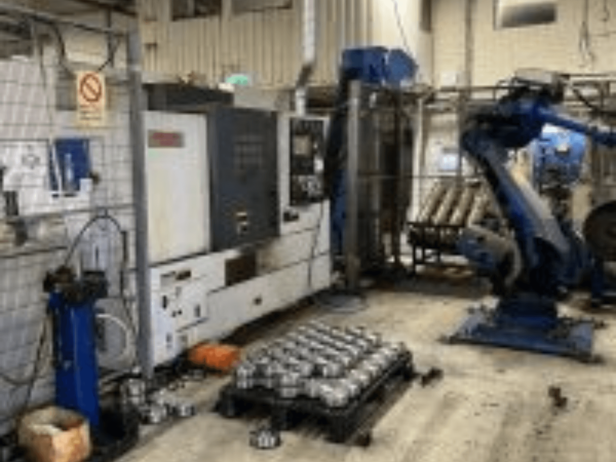 Vista orizzontale del tornio MORI SEIKI NL 2500 MC/700 con braccio robotico e pezzi metallici sul pavimento.