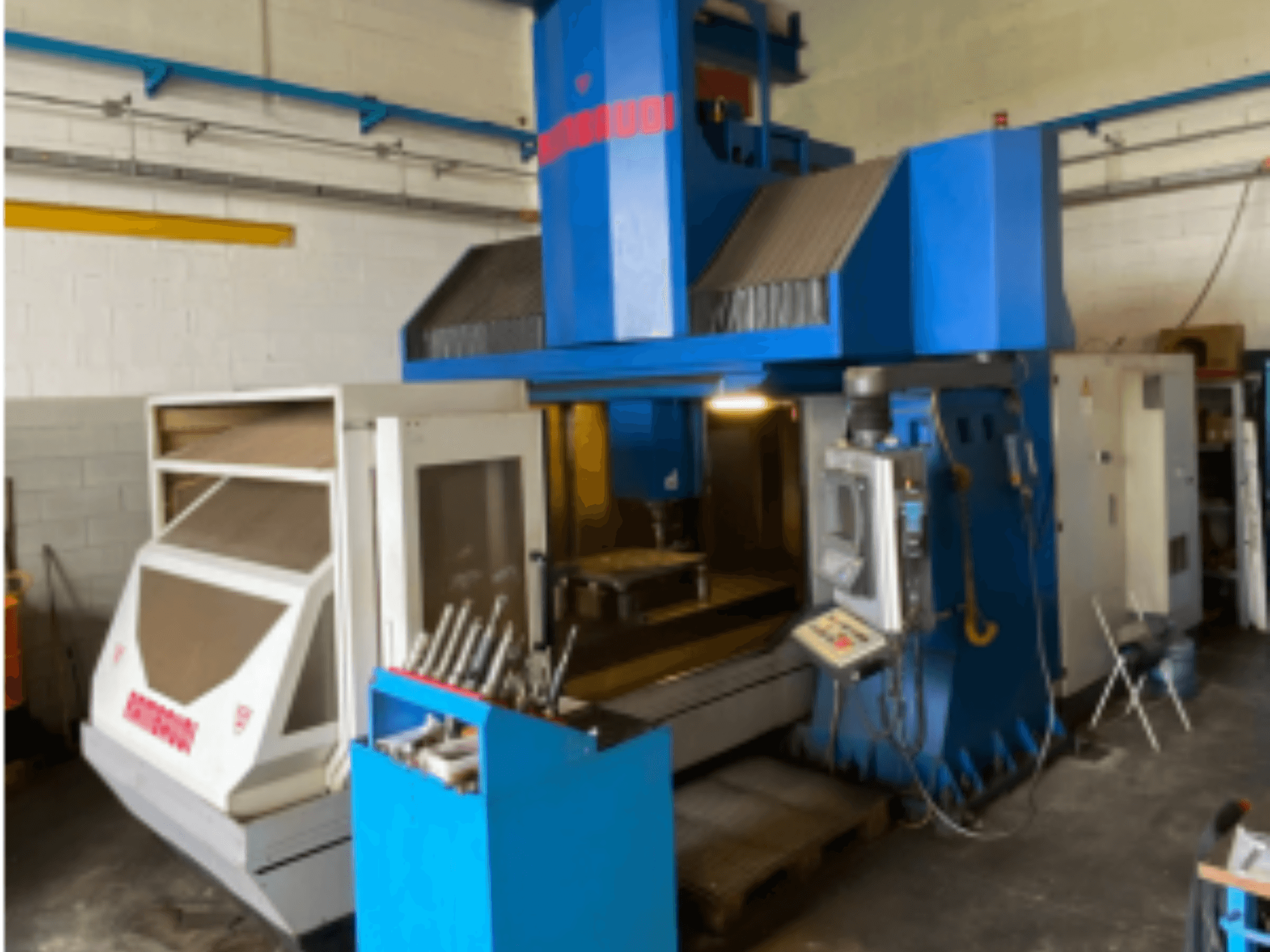 Centro di lavoro verticale Rambaudi RF103, vista frontale che mostra i comandi, il magazzino utensili e l'area di lavorazione. Esterno blu e bianco.