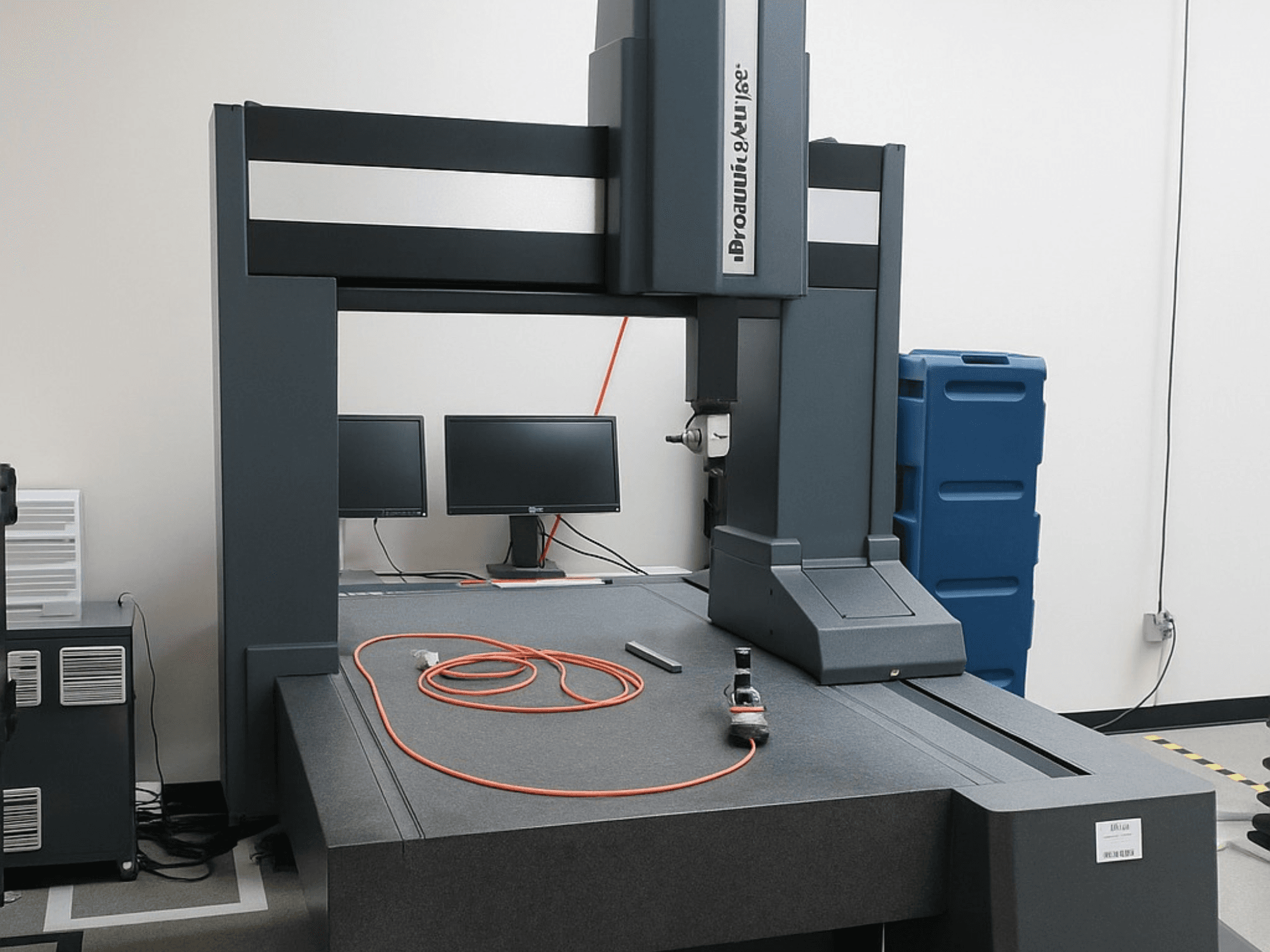 Macchina di misura a coordinate di Brooks Automation con due monitor, vista frontale, con piano grigio e strumenti di misura.