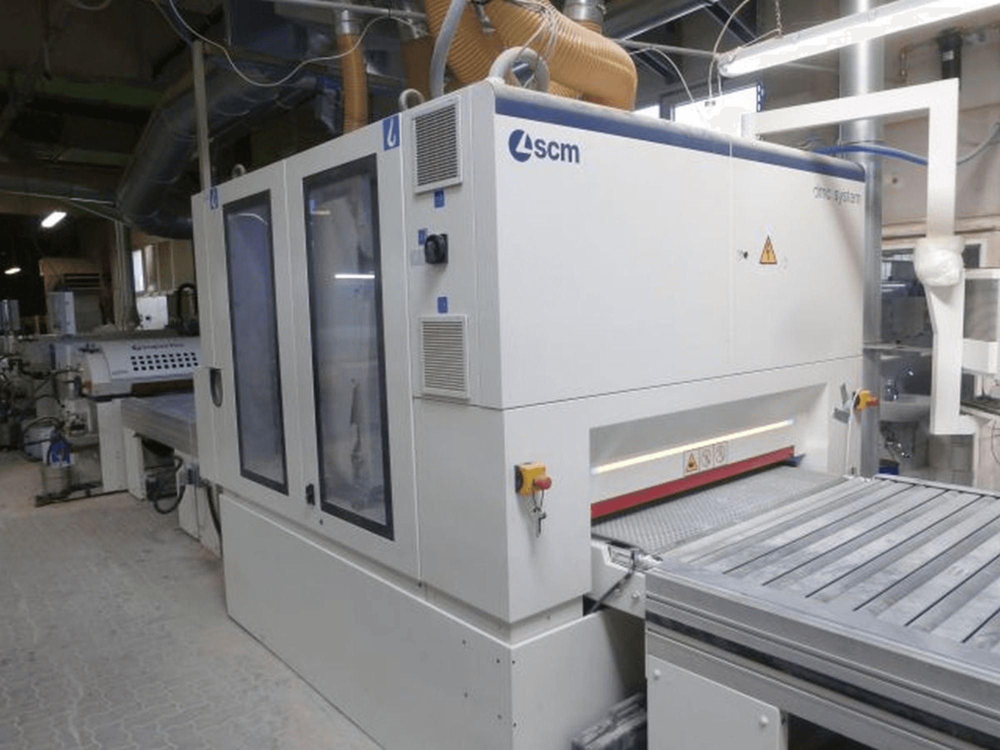 Levigatrice a nastro SCM DMC SY TC 1350 in un'officina, vista laterale che mostra il pannello di controllo e la superficie di levigatura con i dispositivi di sicurezza.