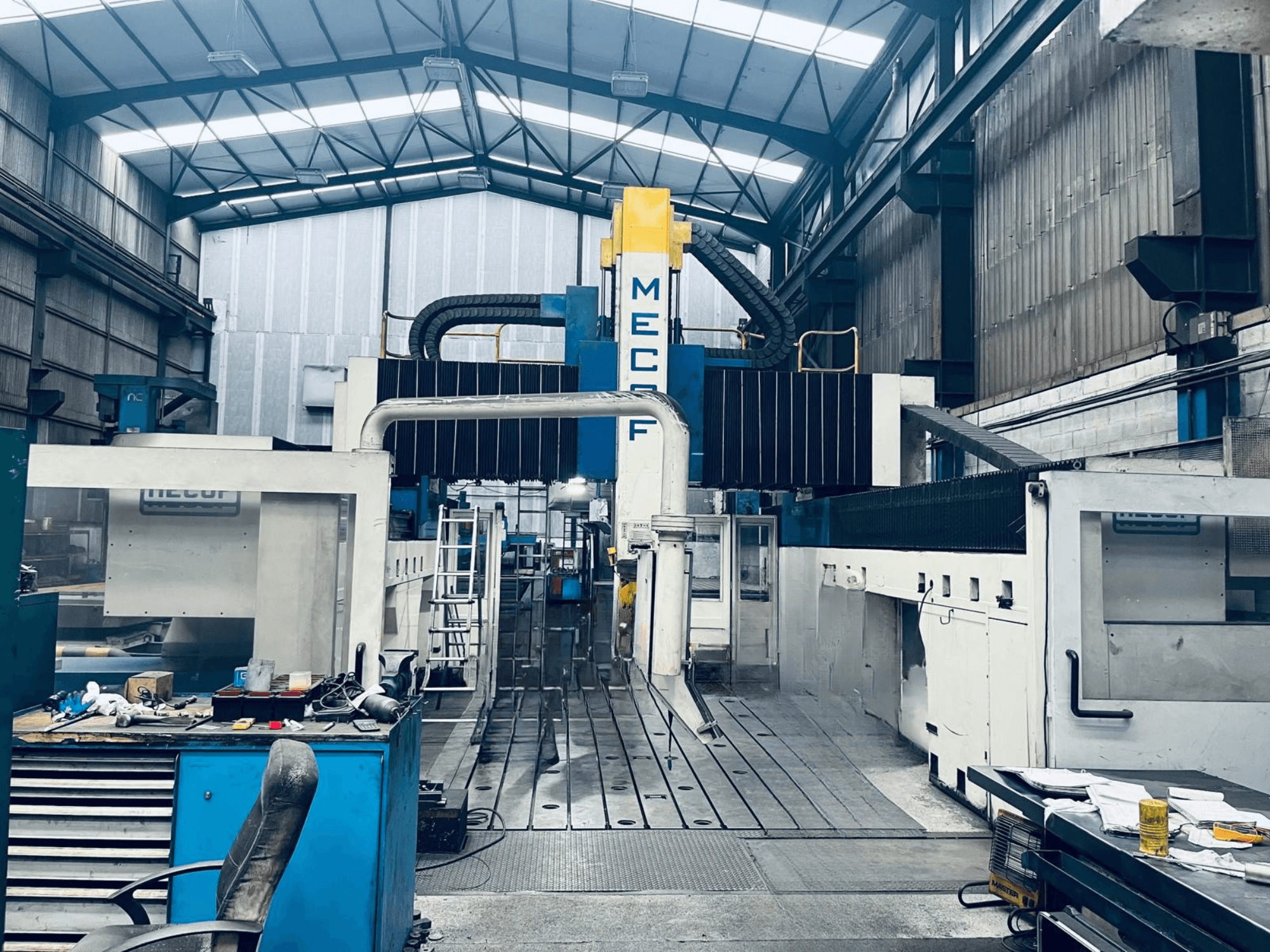 Fresatrice a portale MECOF DYNAMILL 3000L in officina, vista frontale, che mostra la struttura blu e bianca, gli utensili e l'area di lavoro.