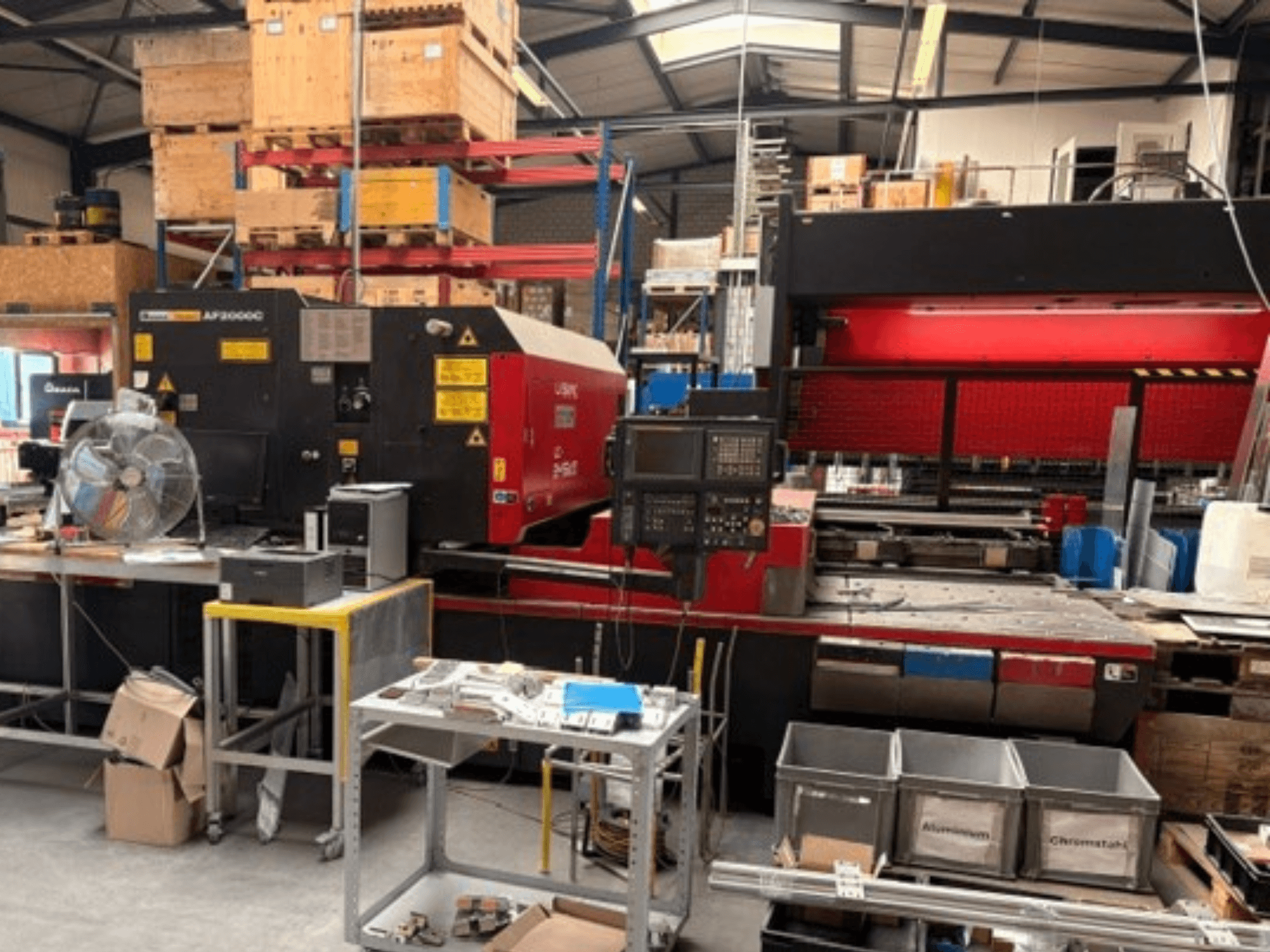 Macchina per il taglio laser a CO₂ AMADA LC-2415αIII in un ambiente di officina, con vista frontale, pannello di controllo e area operativa.