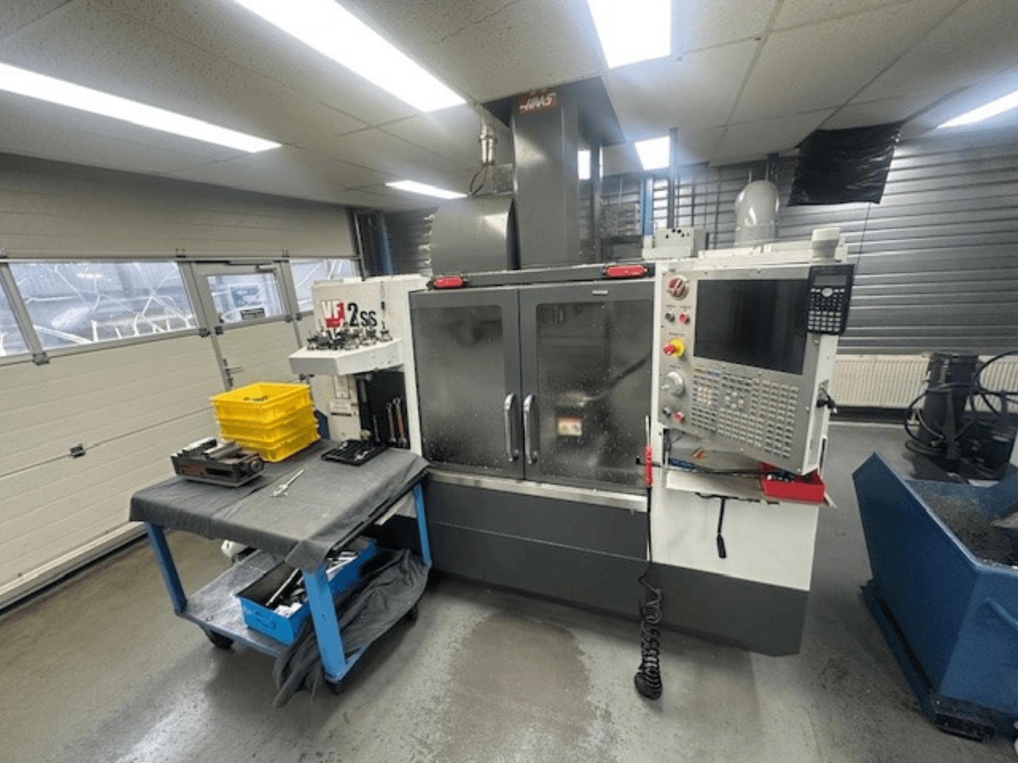 Vista frontale del centro di lavoro verticale HAAS VF-2SS con pannello di controllo, piano di lavoro e stazione di stoccaggio utensili.