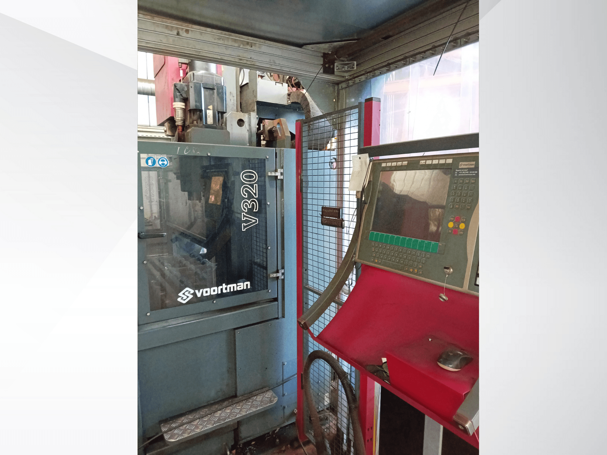 Vista frontale della macchina CNC Voortman V320, con pannello di controllo con pulsanti, schermo di visualizzazione e copertura in rete di sicurezza.