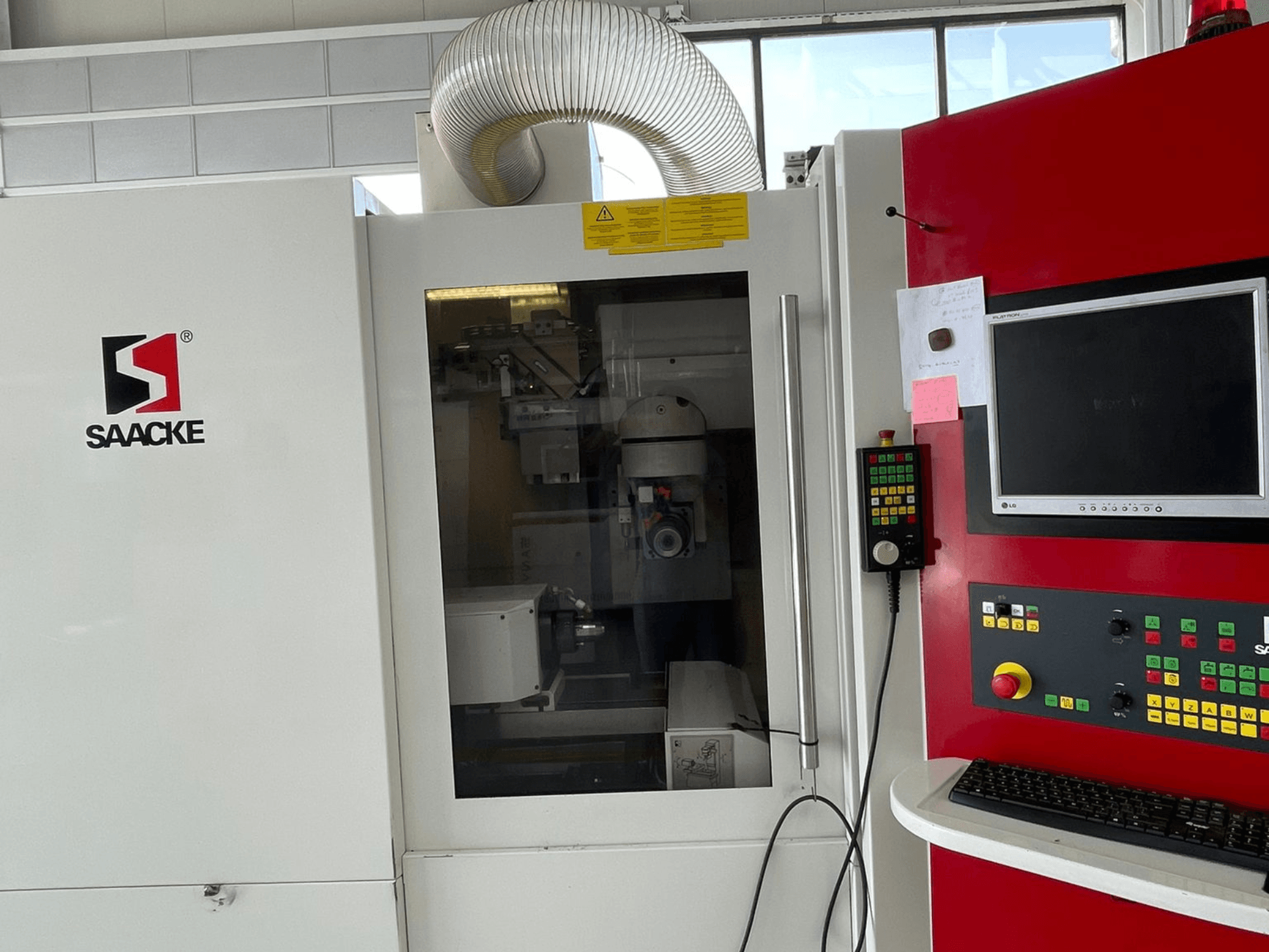 Macchina SAACKE in bianco e rosso, vista frontale, con pannello di controllo, monitor e parti interne visibili attraverso il vetro.