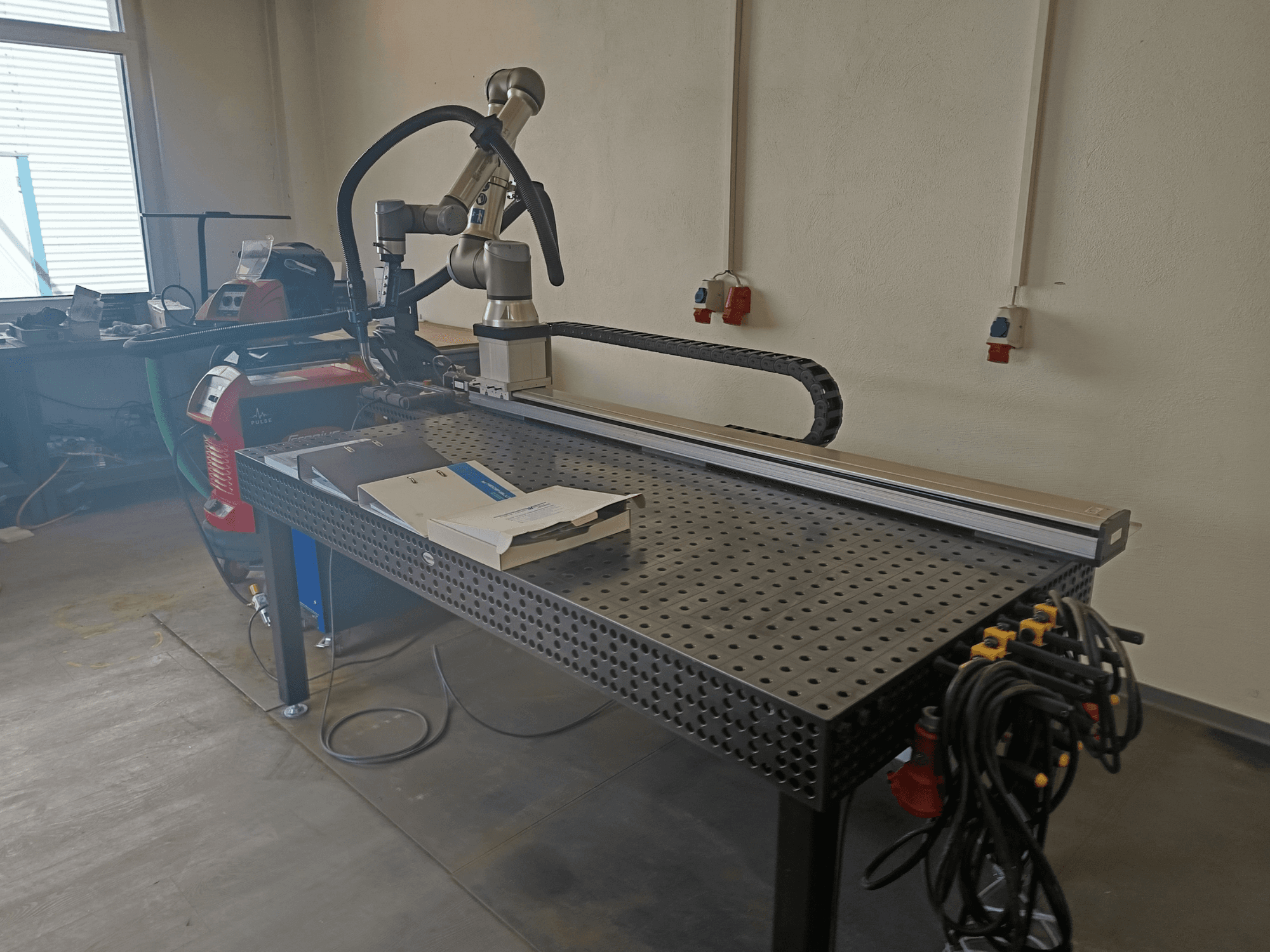 Cella di saldatura a impulsi FRONIUS TransSteel 4000 vista di lato, dotata di braccio robotico, area di lavoro e collegamenti elettrici.