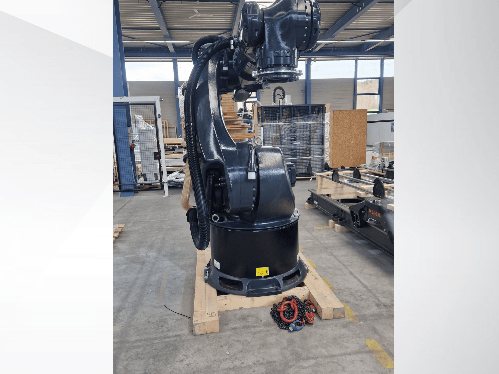 Braccio robotico KUKA KR 340 R3330 in un magazzino, vista laterale che ne mostra la base e i cavi, con delle catene in primo piano.
