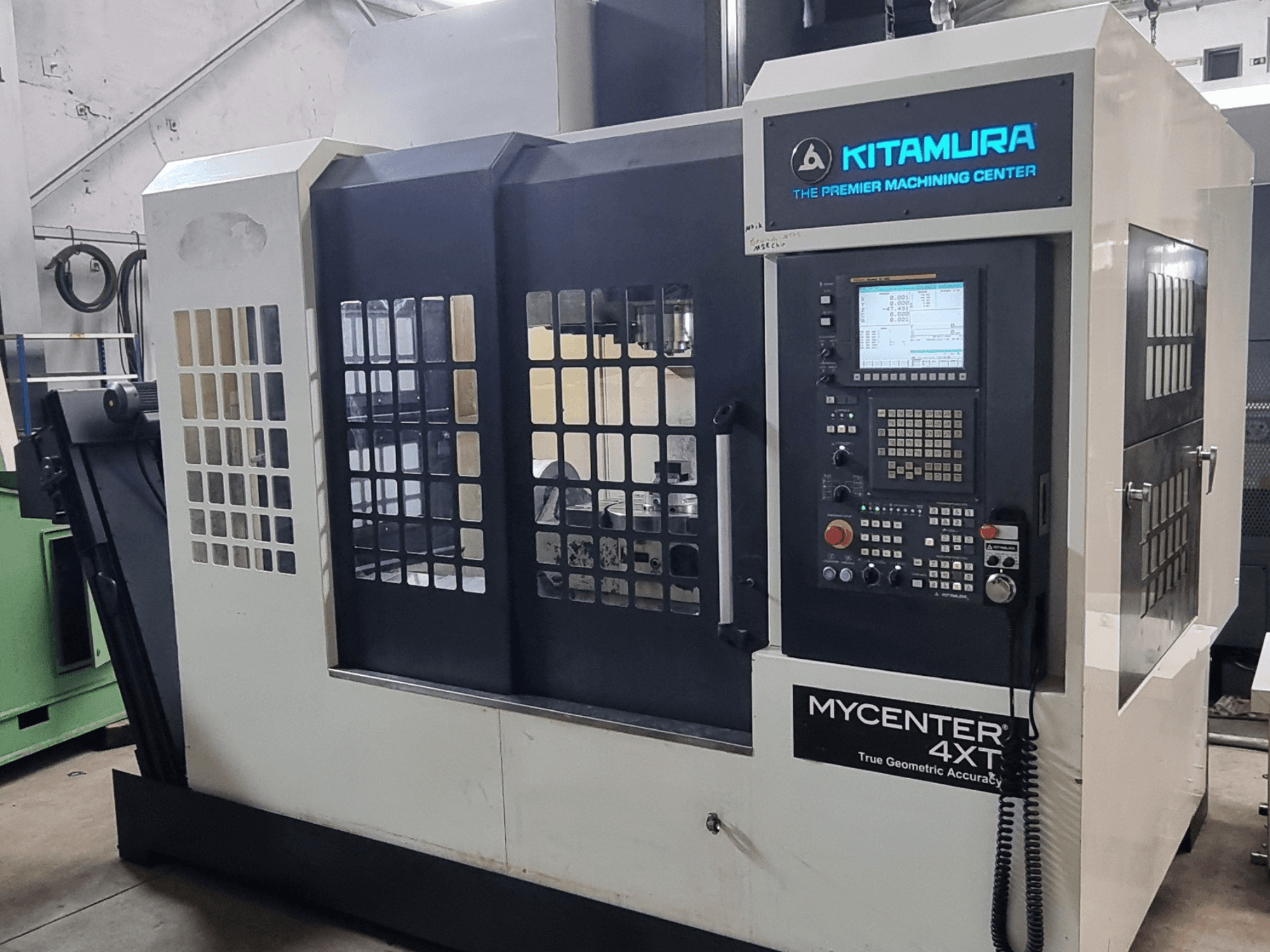 Testo alternativo: Centro di lavorazione verticale Kitamura MYCENTER 4XT, vista frontale, con in primo piano il pannello di controllo e i dettagli della macchina in un ambiente di officina.