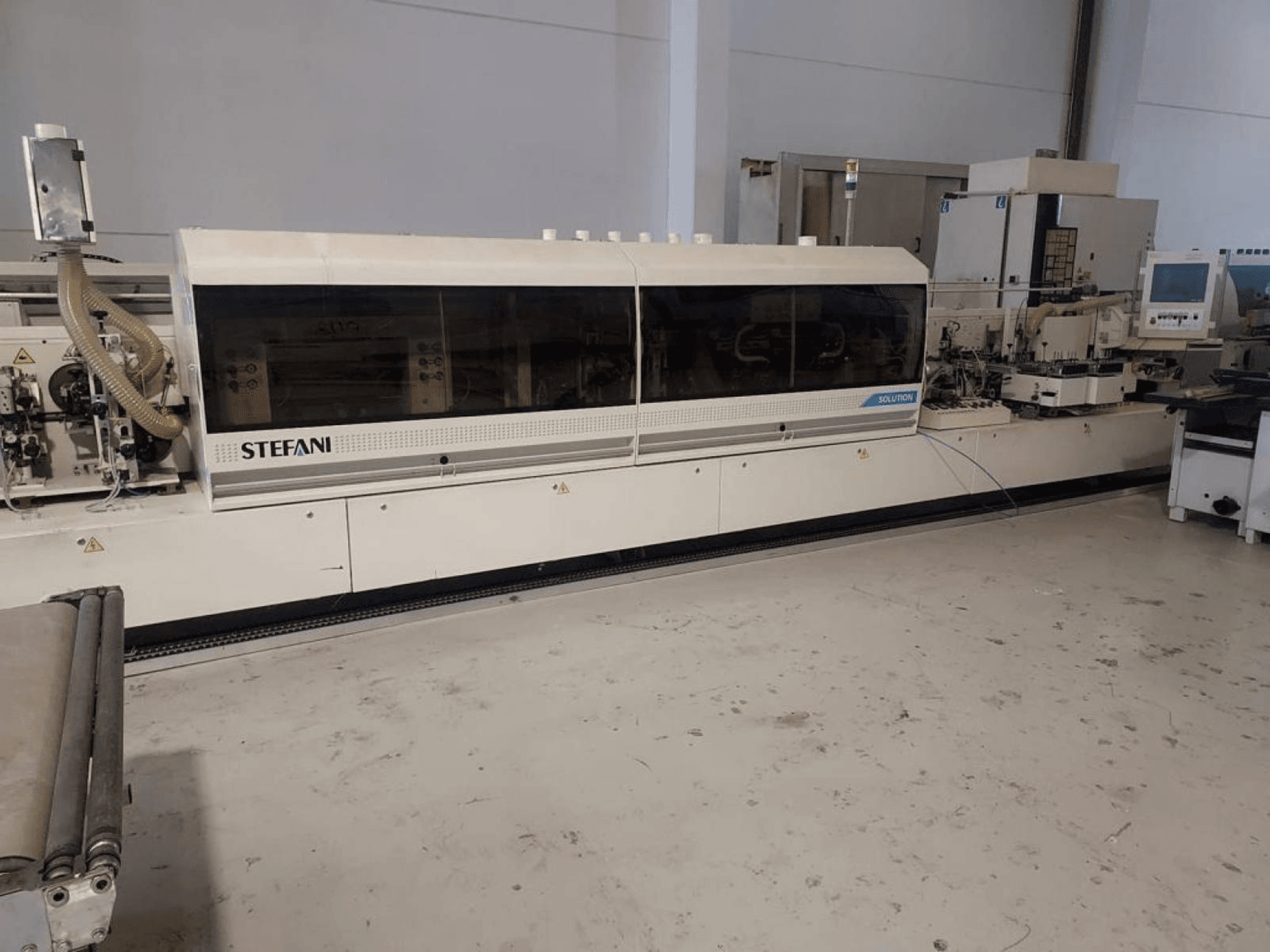 Macchina bordatrice Stefani Solutions, vista frontale, con sistema di aspirazione della polvere e pannello di controllo visibili, in un'officina.