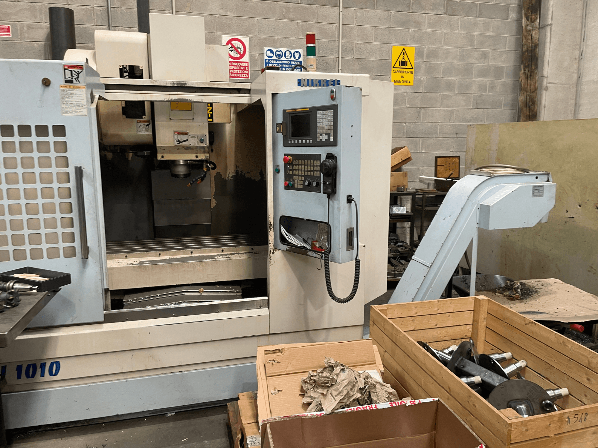 Centro di lavoro verticale di Other, modello VH-1010, visto dal davanti con i comandi visibili e le scatole vicine.