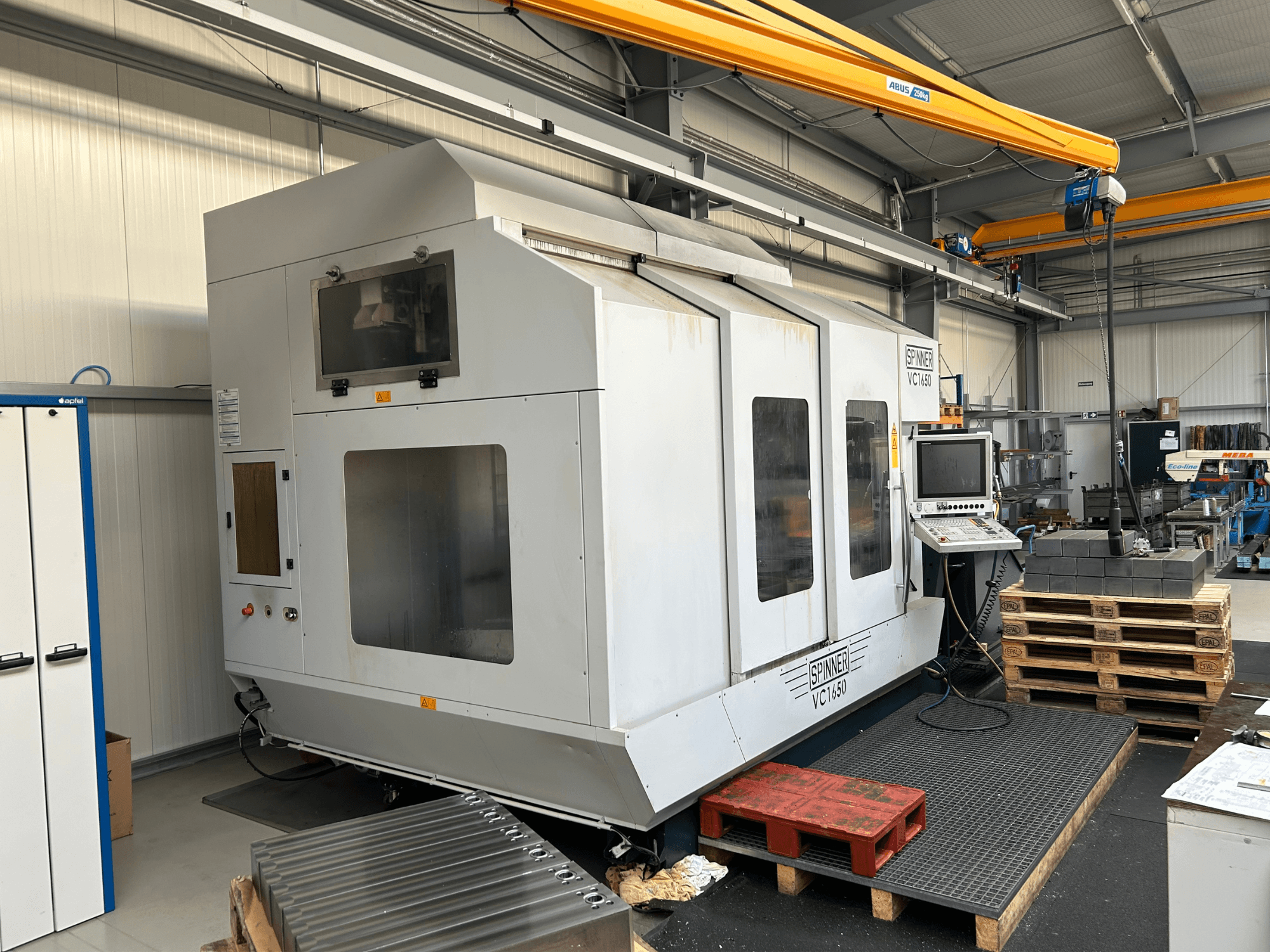 Macchina CNC Spinner VC 1650, vista frontale, con pannello di controllo, ampie finestre e pallet impilati nelle vicinanze in un'officina.