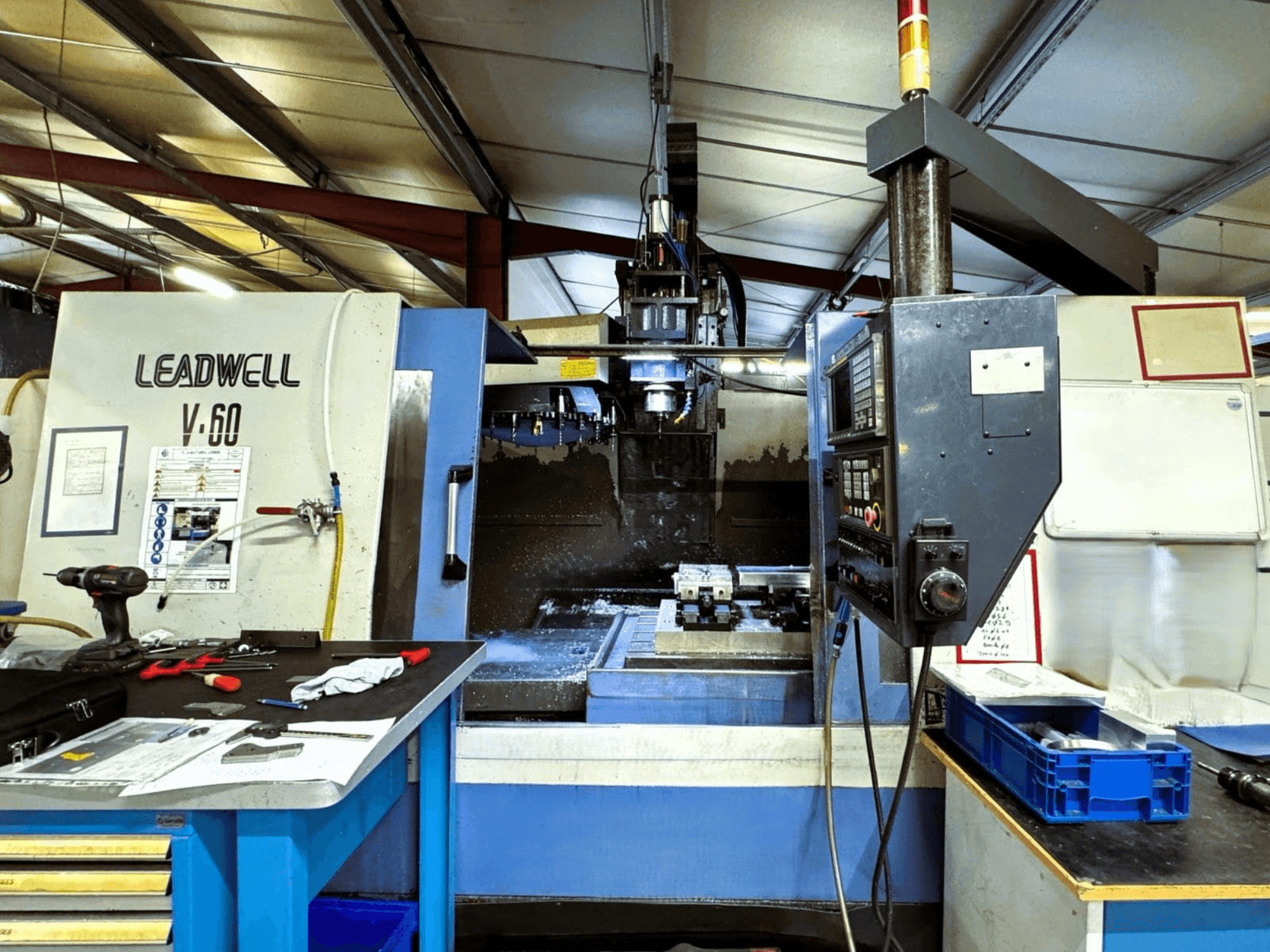 Centro di lavorazione verticale Leadwell V-60 visto di lato, con in primo piano il pannello di controllo e l'area di lavoro con utensili e pezzi.