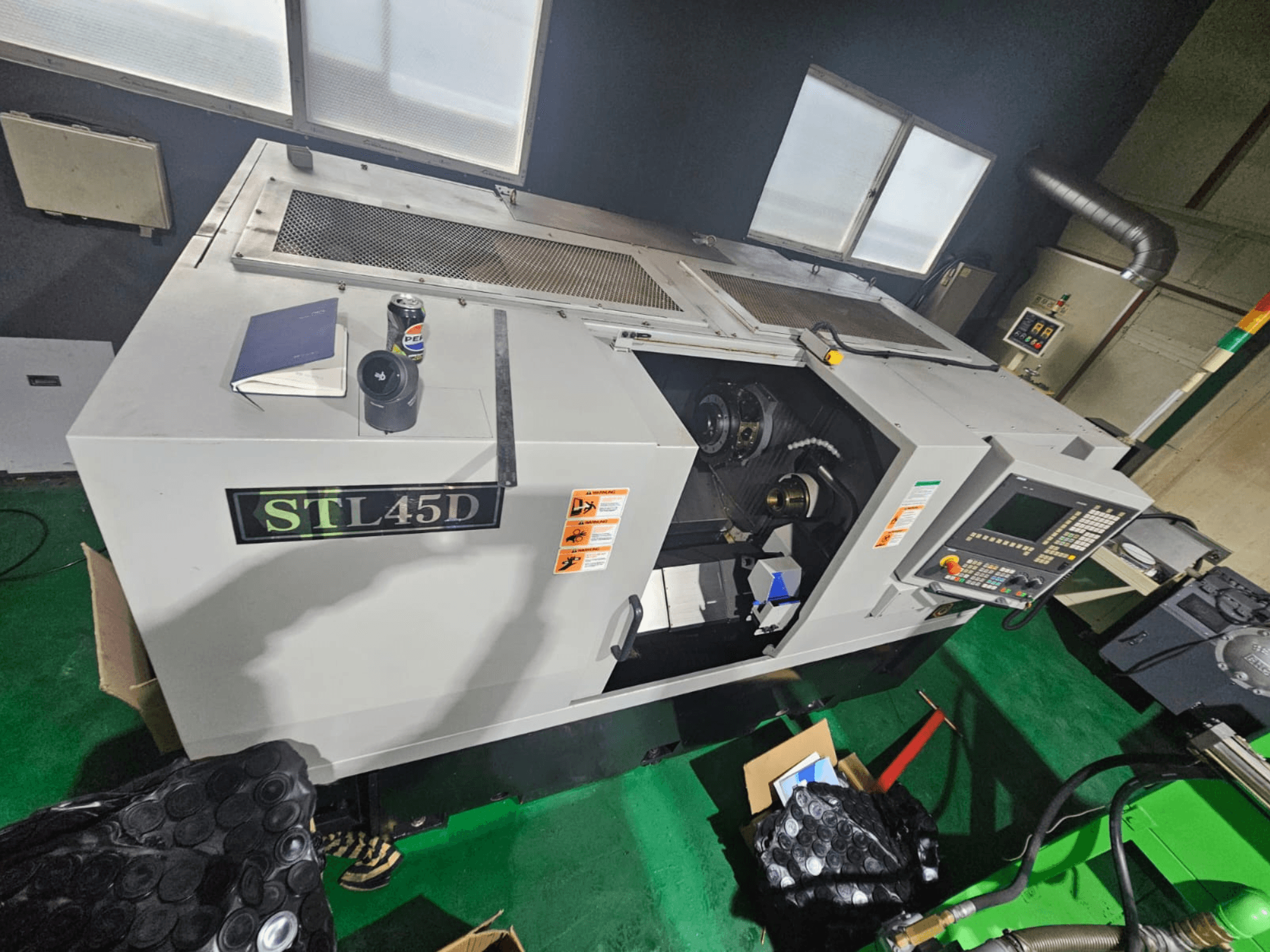 Macchina CNC STL45D vista dall'alto, con il pannello di controllo, il pezzo cilindrico, il notebook e la lattina in alto.