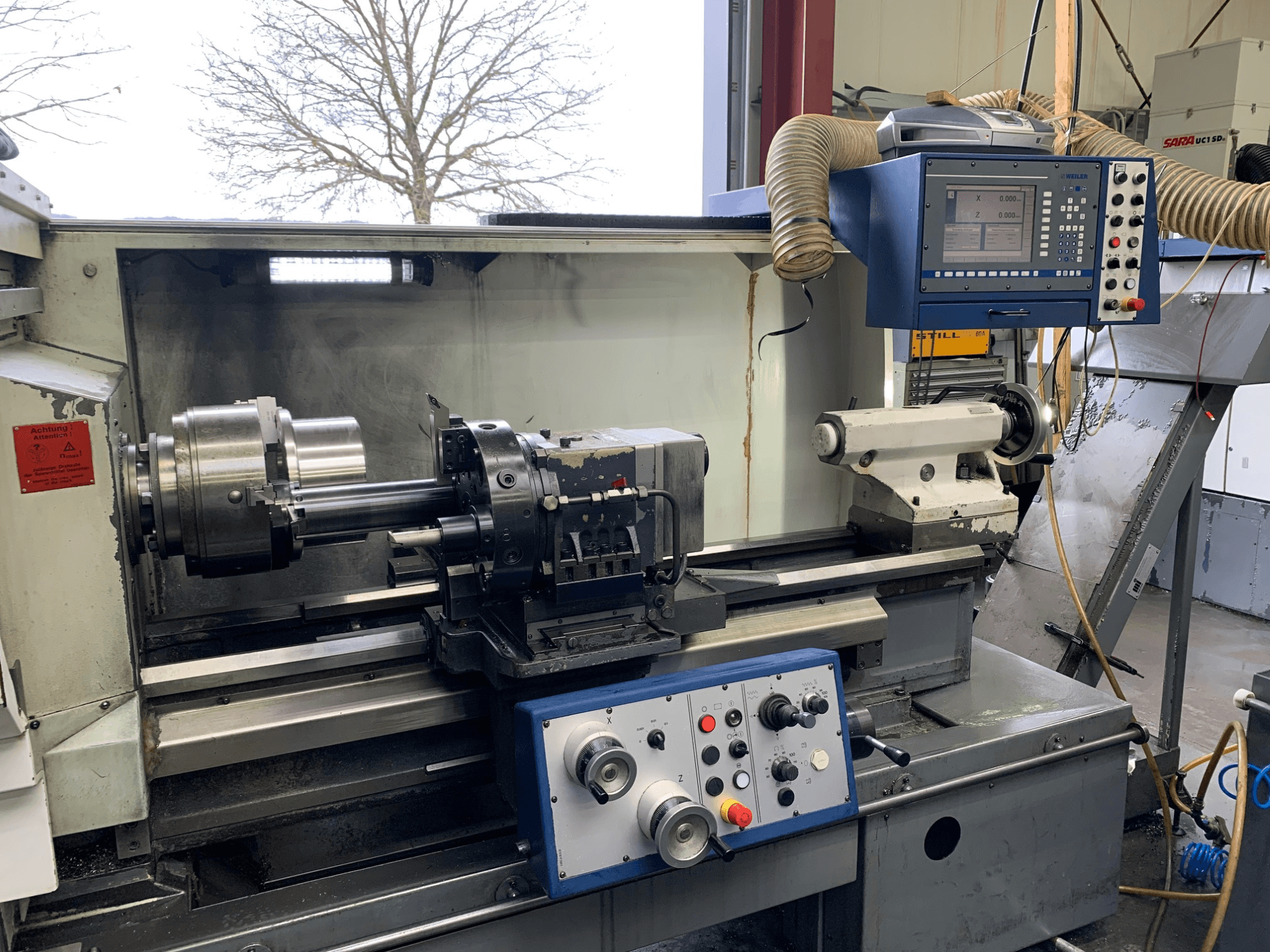 Tornio orizzontale Weiler E55X1000 in un'officina, con pannello di controllo, tornio e portautensili. Vista frontale.