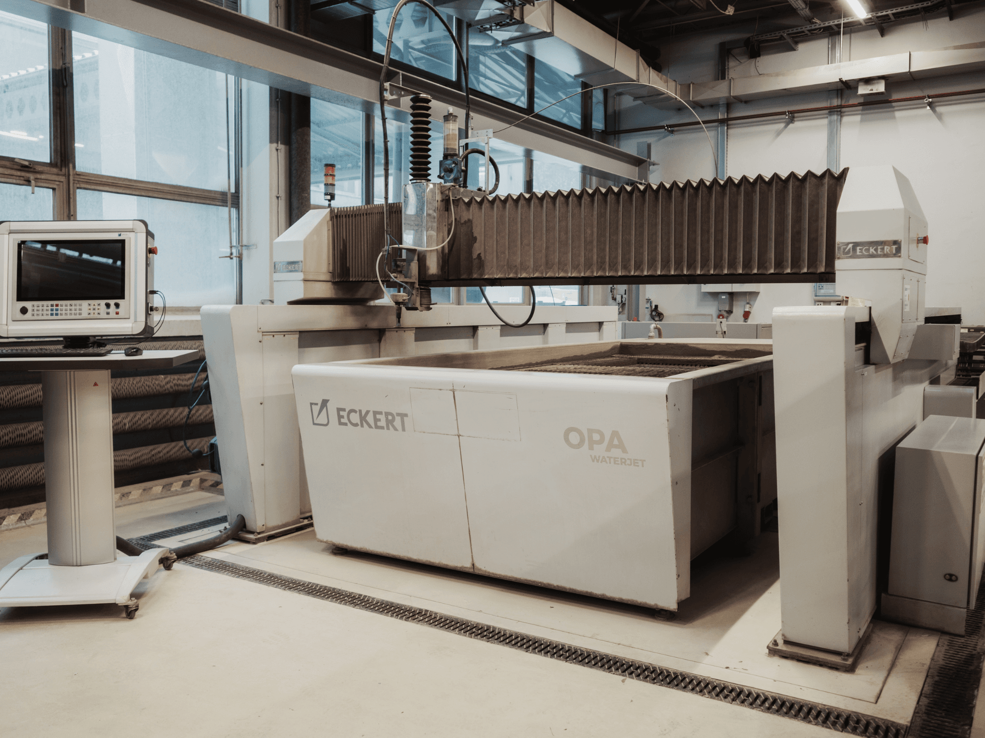 Macchina da taglio a getto d'acqua ECKERT OPAL in un'officina, vista frontale con la console di comando nelle vicinanze.
