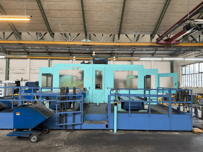 Macchina industriale a controllo numerico di colore blu con pannelli di protezione, vista frontale, dotata di magazzino utensili e carrello di raccolta rifiuti sul lato.