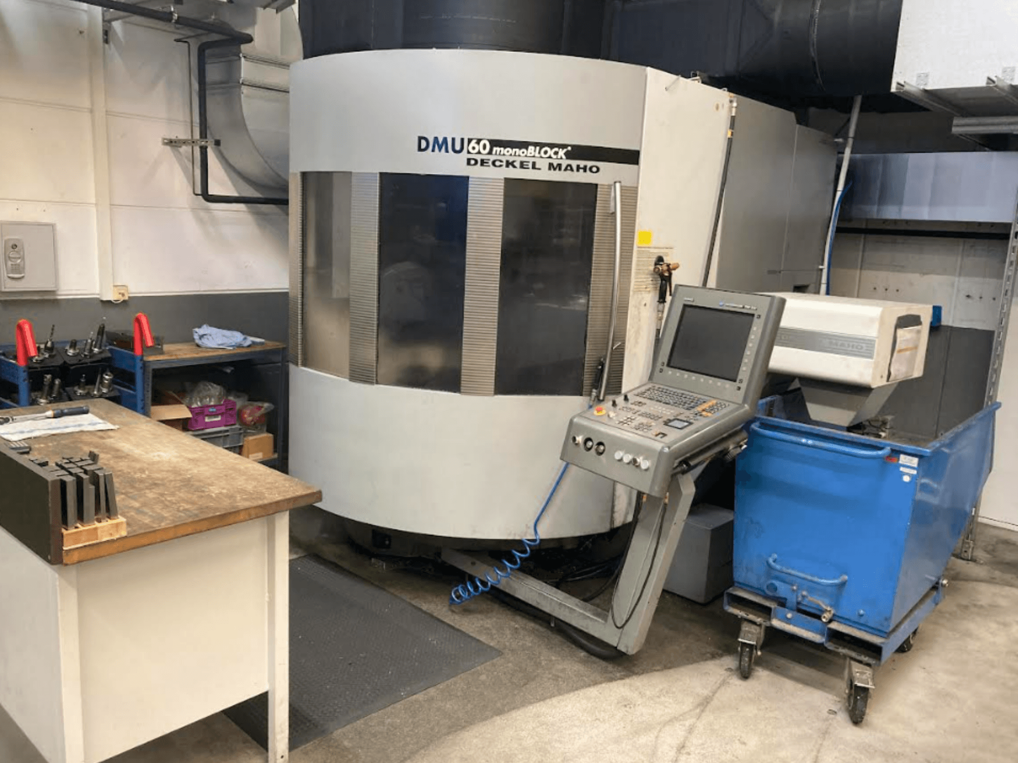 Centro di lavoro verticale DMG MORI DMU 60 Monoblock, vista frontale con pannello di controllo, area di lavoro e carrello portautensili blu visibili.