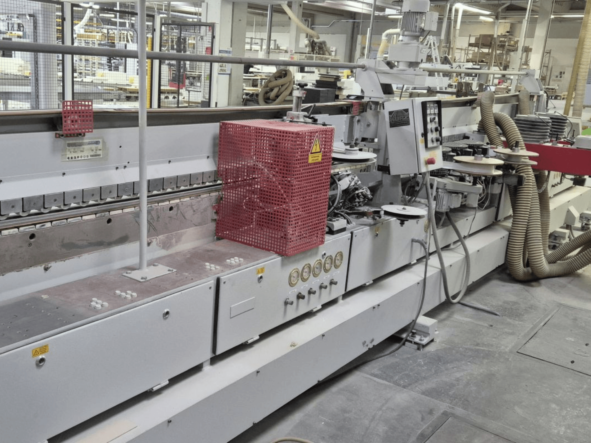 Macchina bordatrice con pannello di controllo, tubi di aspirazione e copertura di sicurezza rossa, vista da un'angolazione laterale.