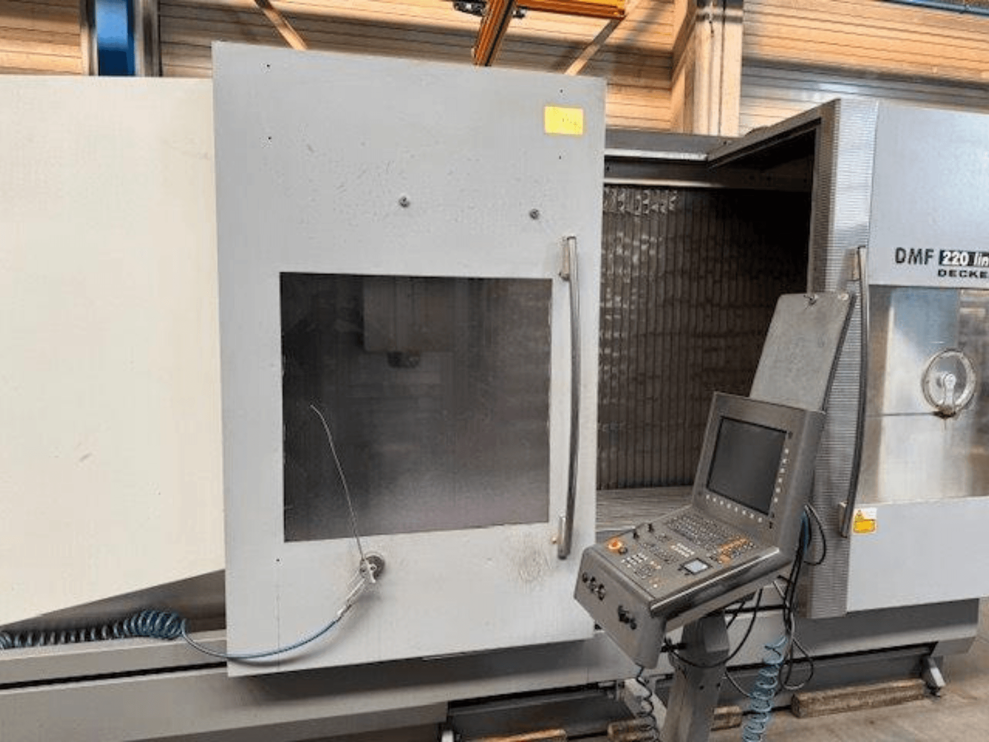 Vista frontale del centro di lavoro verticale lineare DECKEL MAHO DMF 220, che mostra il pannello di controllo e la porta aperta della macchina.