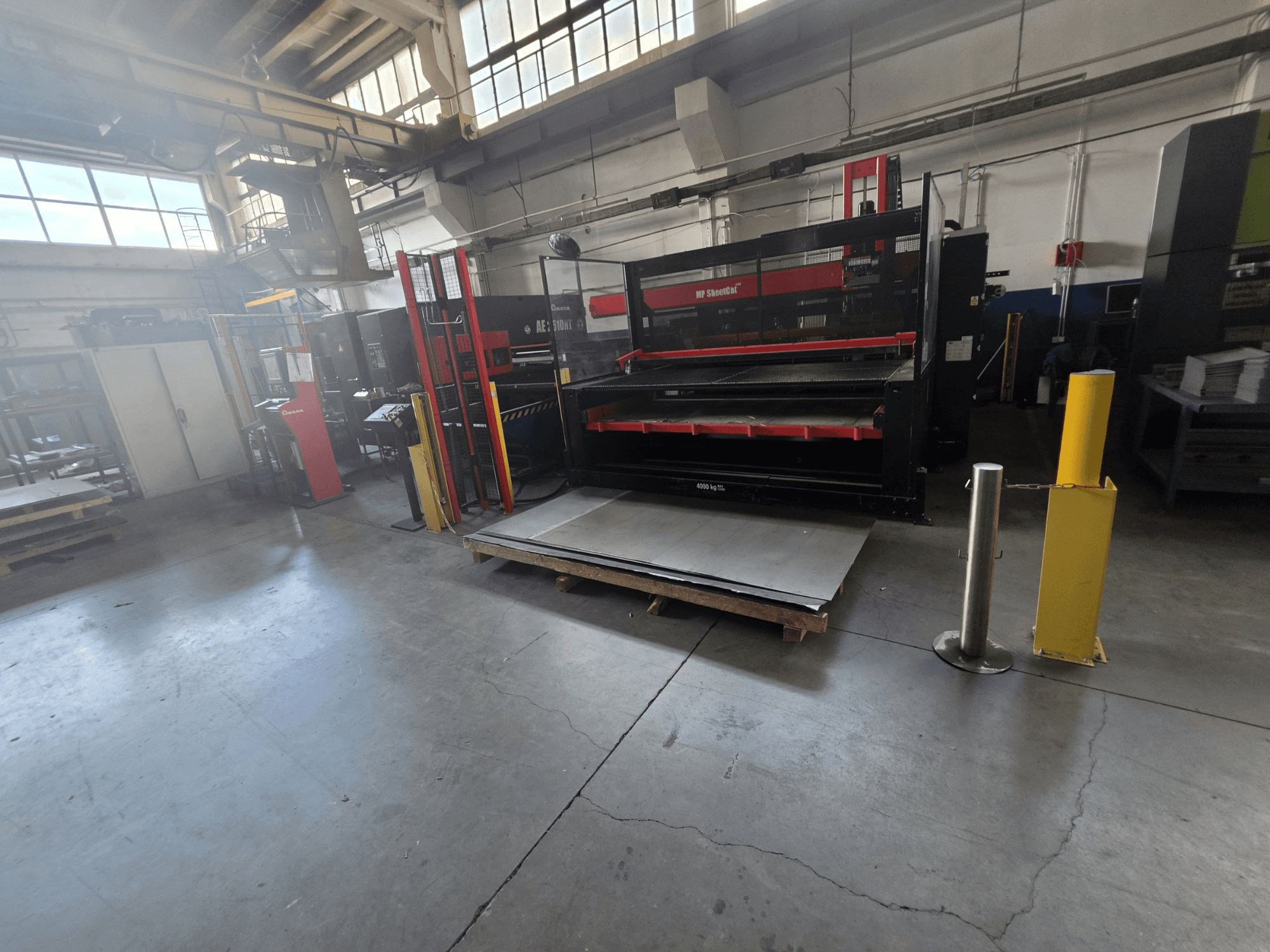 Punzonatrice CNC AMADA AE-2510NT in magazzino, vista di profilo, che mostra la configurazione della macchina e le lamiere.