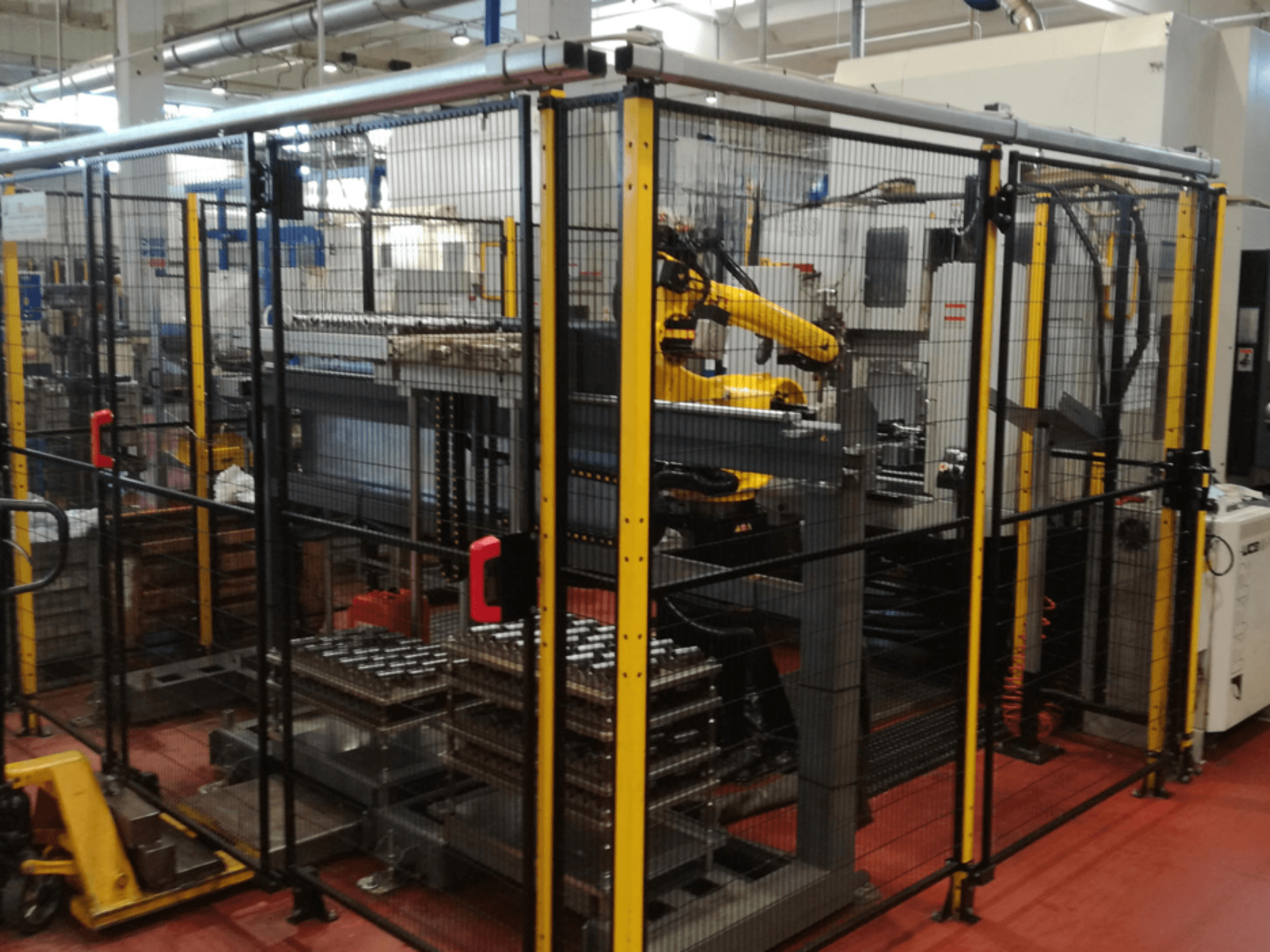 Centro di lavoro verticale Enshu EV450 in uno spazio di lavoro recintato, con bracci robotici e pezzi multipli impilati. Vista frontale.