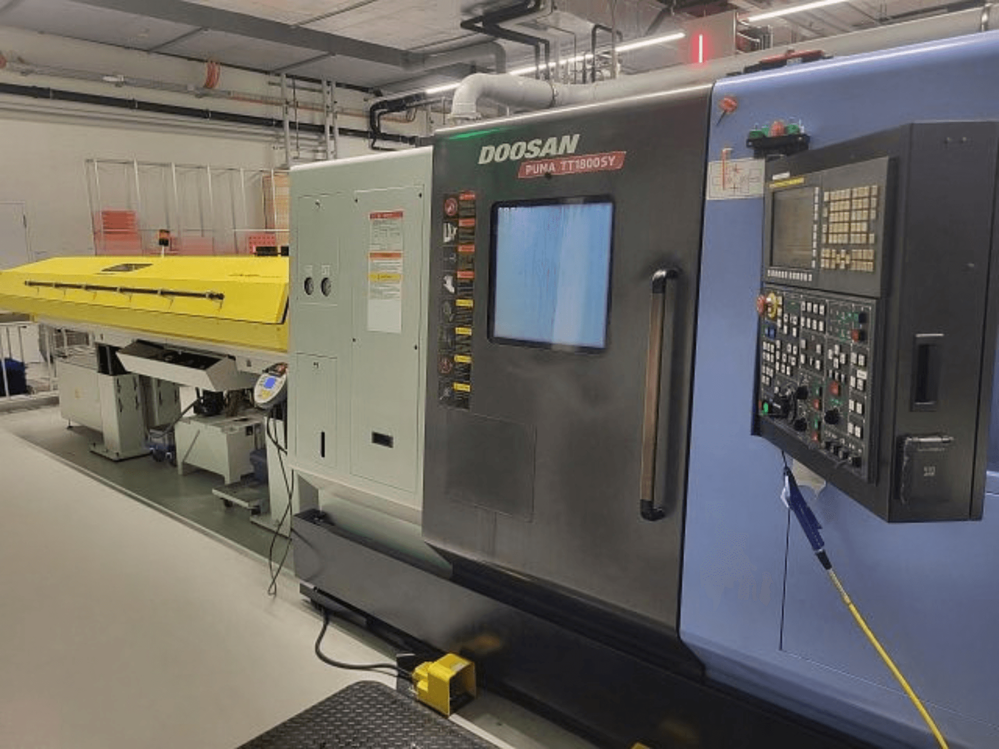 Centro di tornitura e fresatura DOOSAN PUMA TT 1800 SY, vista frontale con pannello di controllo e copertura gialla, ambiente industriale.
