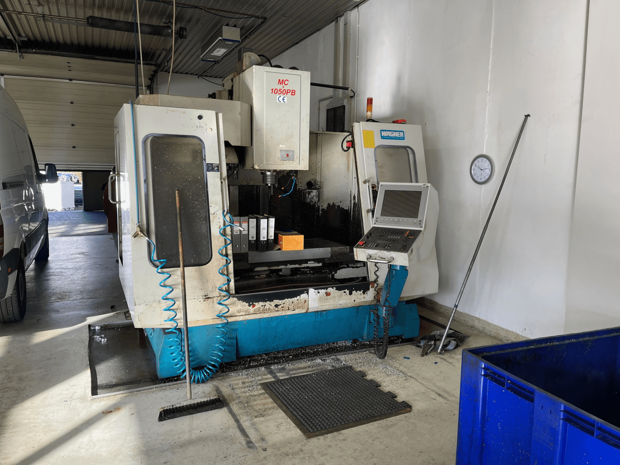 Macchina CNC WAGNER MC 1050PB in officina, vista frontale, con pannello di controllo e area di lavoro; sono visibili il tubo dell'aria blu e gli strumenti di pulizia.