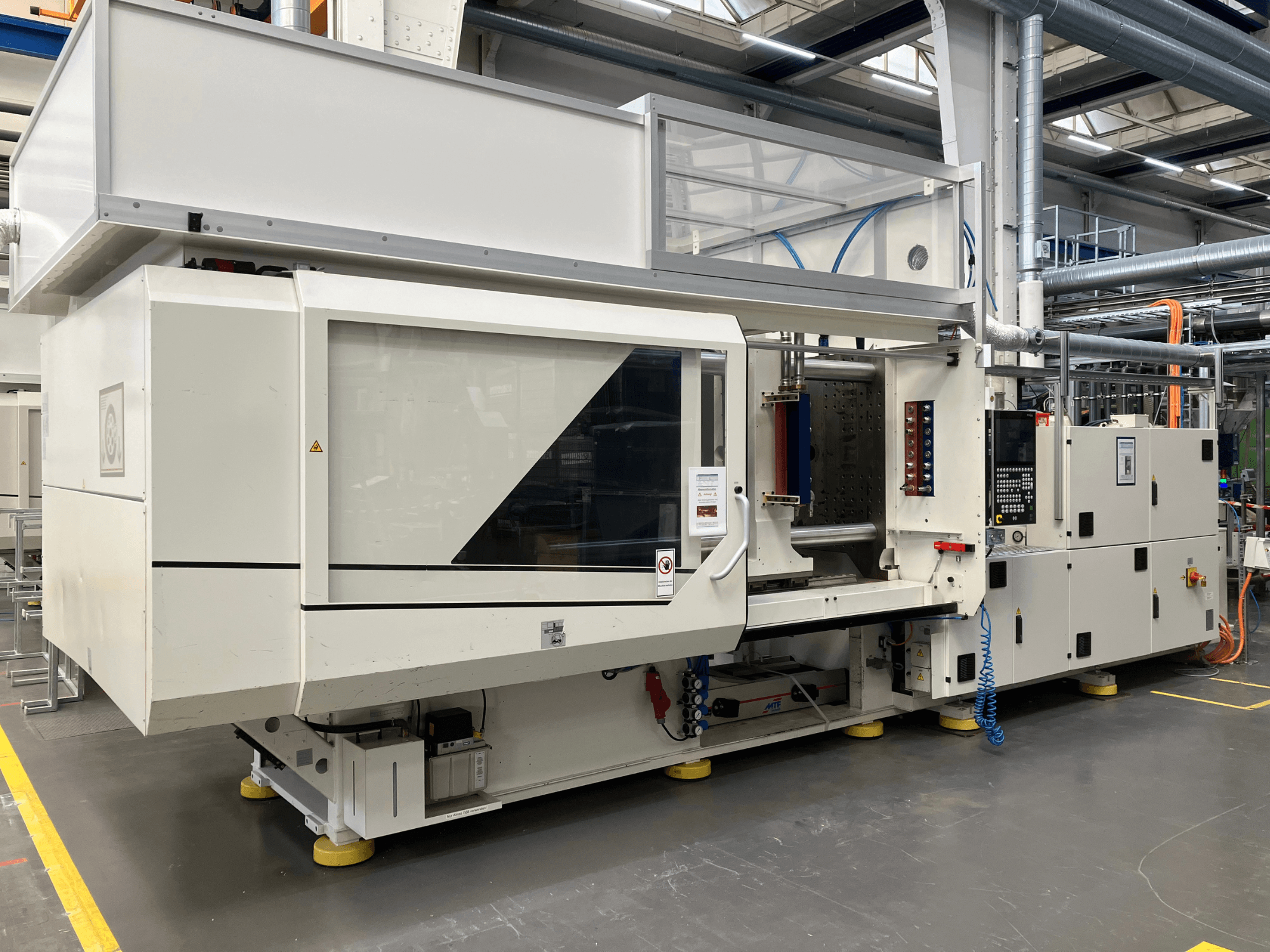 Vista laterale di una pressa a iniezione, modello AET, con pannello di controllo e coperture trasparenti, in un ambiente industriale.